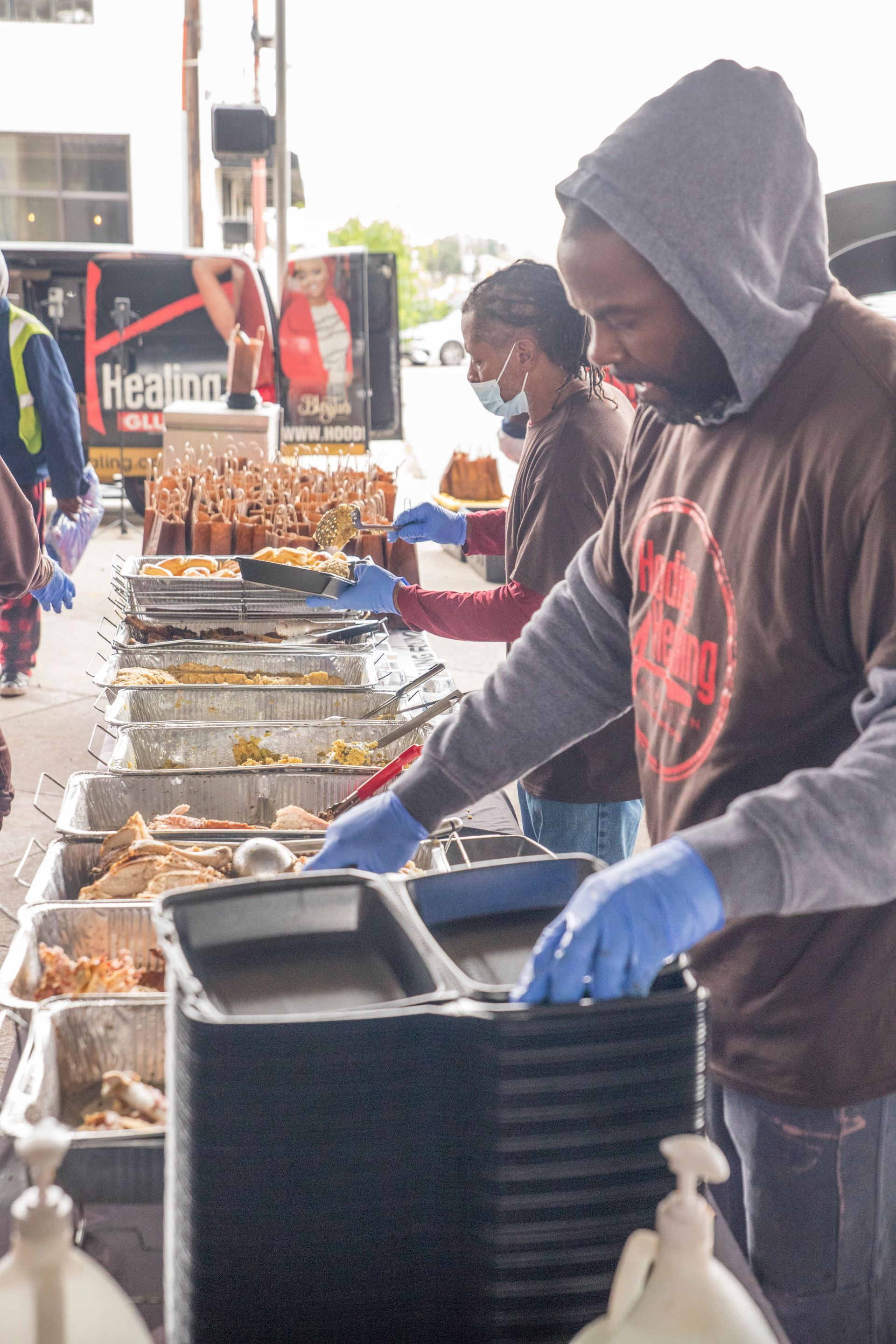 A man in a hooded sweatshirt is preparing food at a buffet table