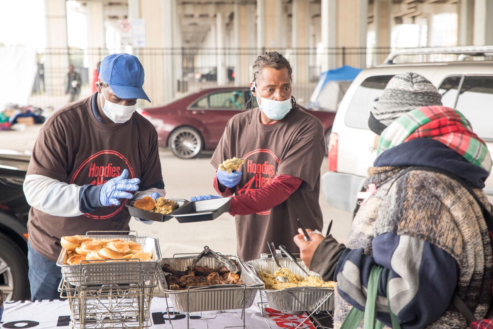 Two men wearing face masks are serving food to a woman.