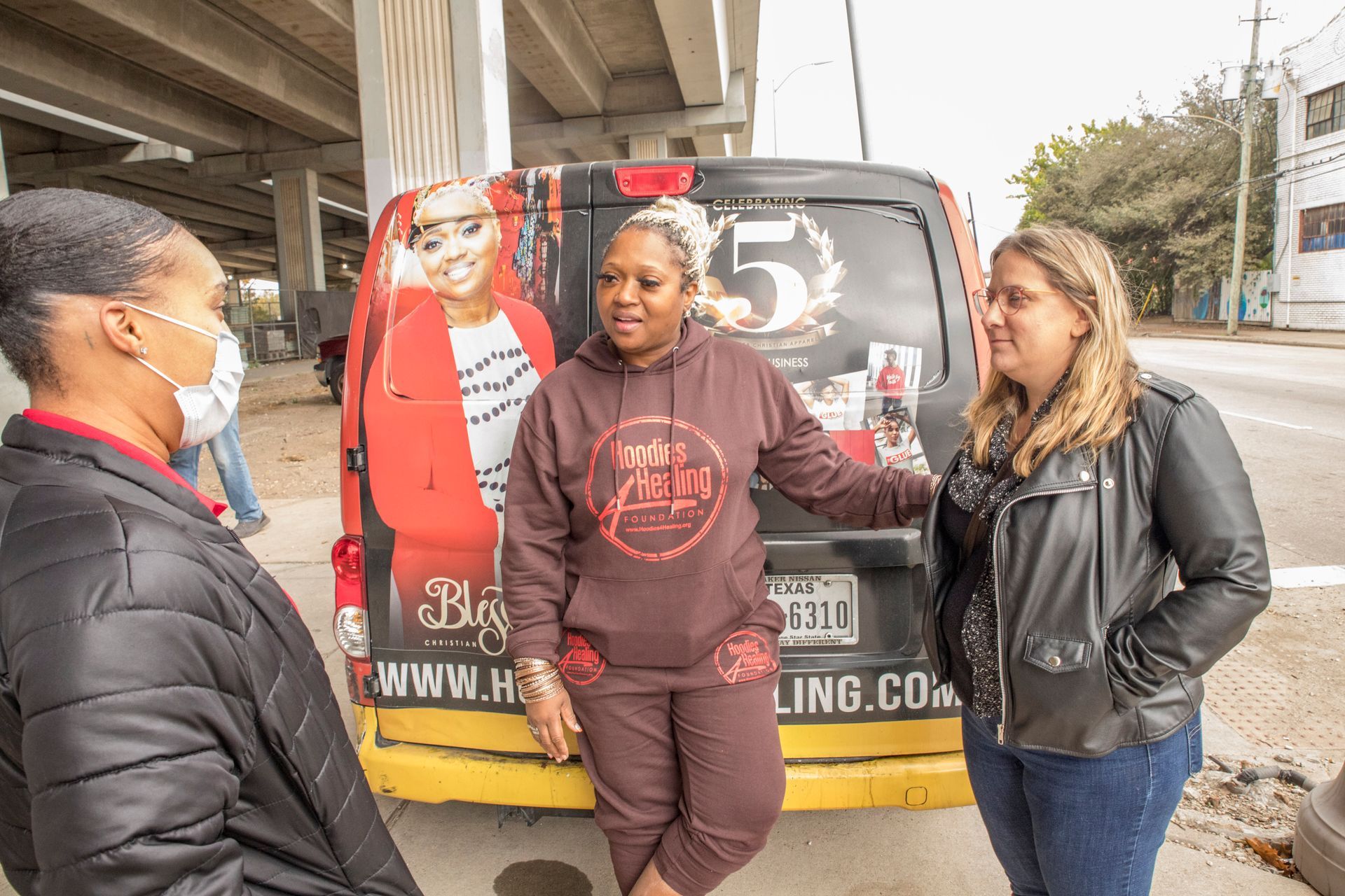 Three women are standing next to a van on the side of the road.