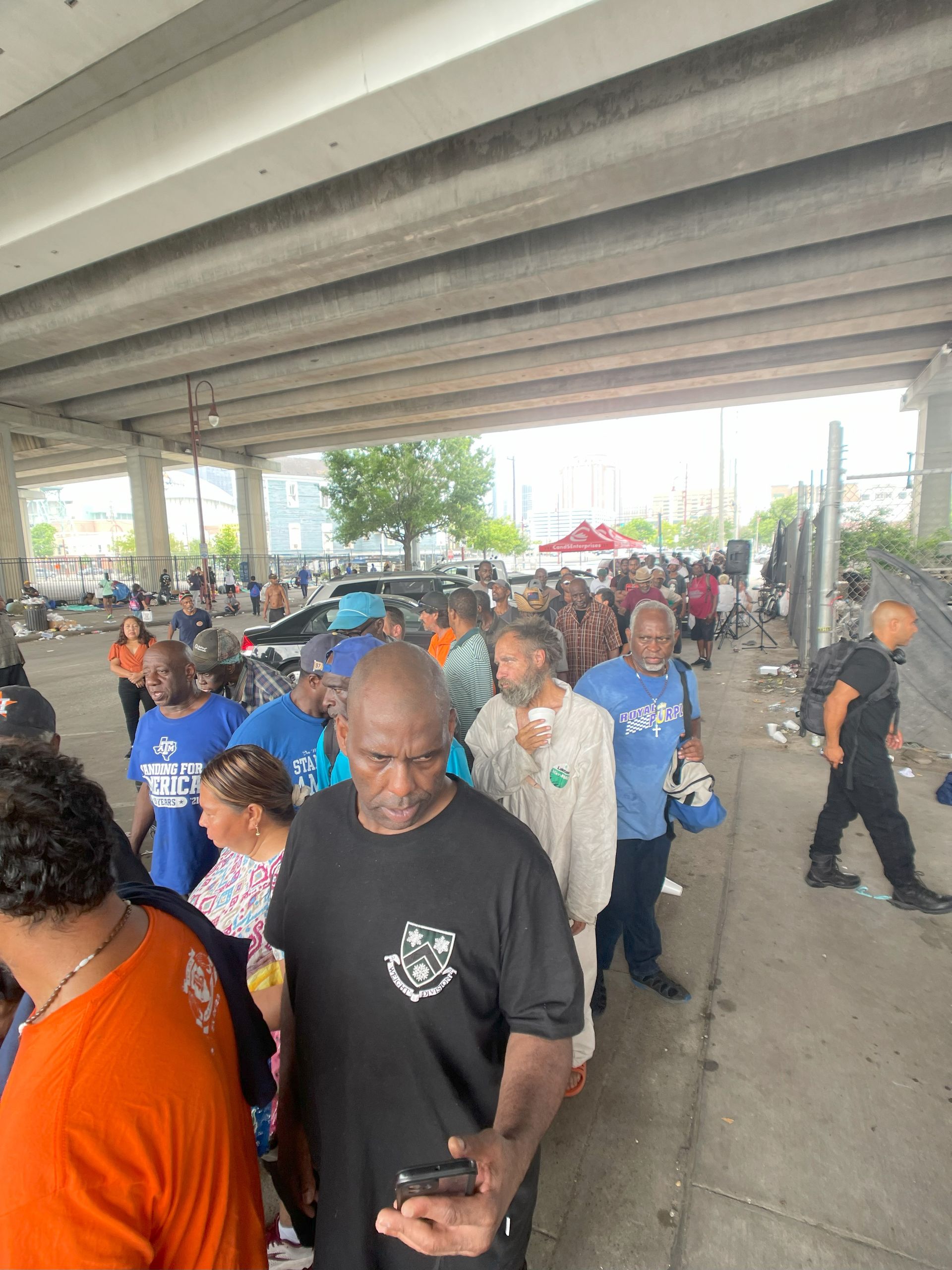 A group of people are standing in a line under a bridge.