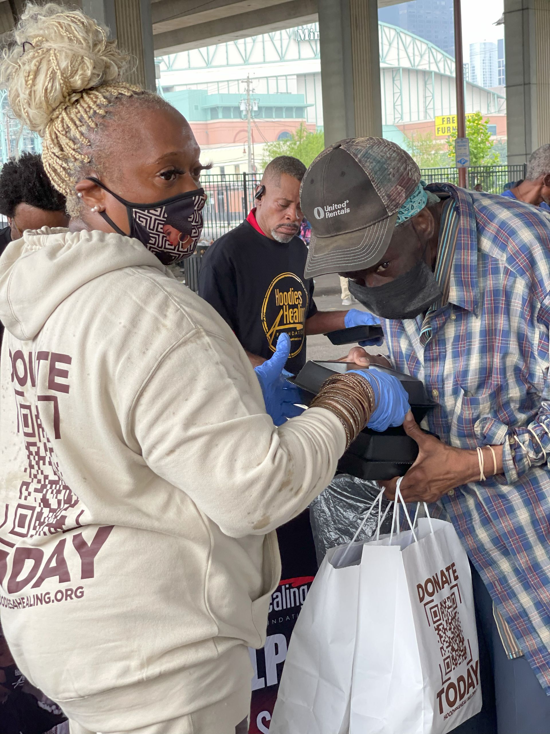 A woman wearing a mask is giving a man a bag of food.