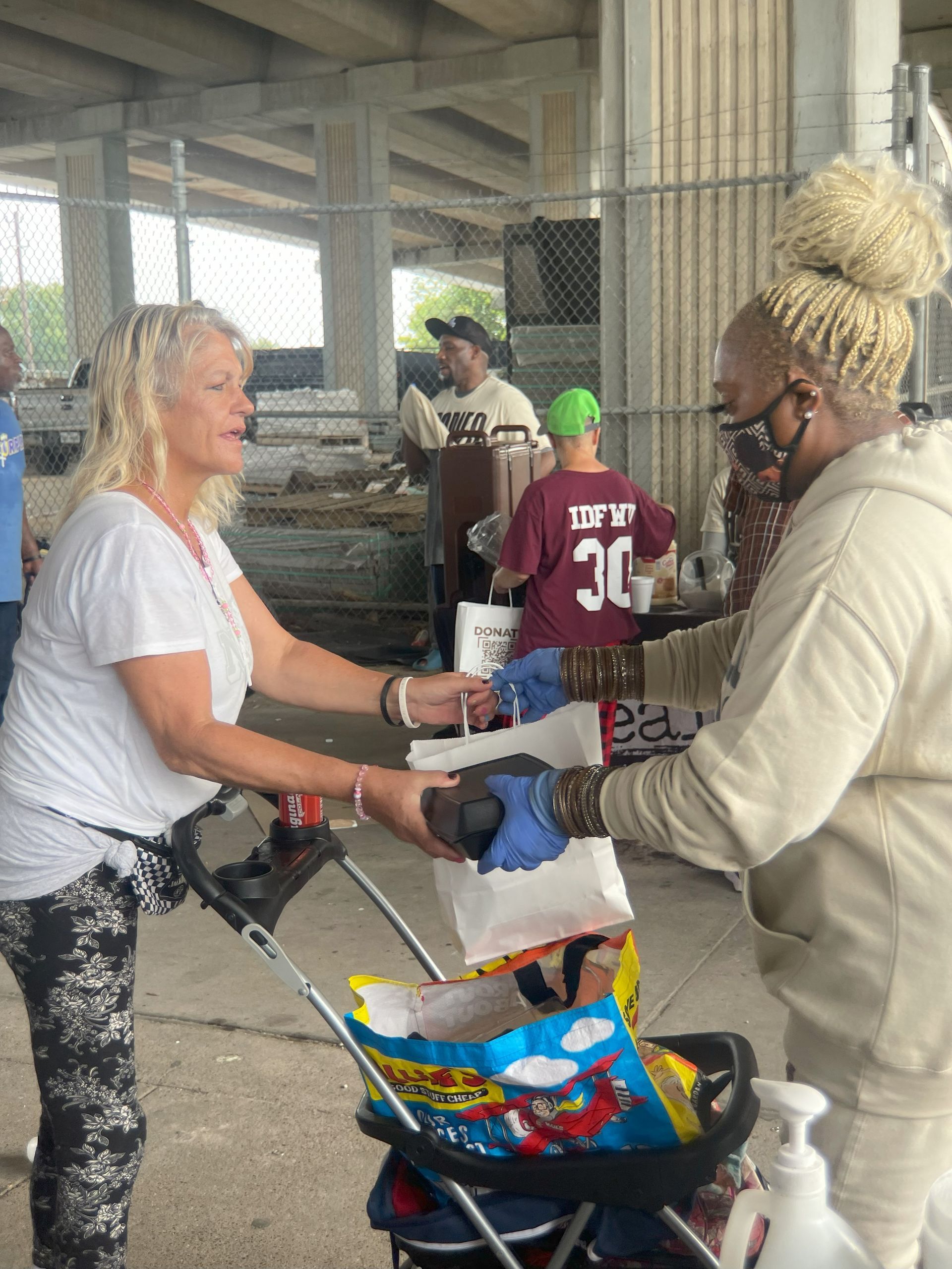 A woman is handing a bag to another woman in a stroller.
