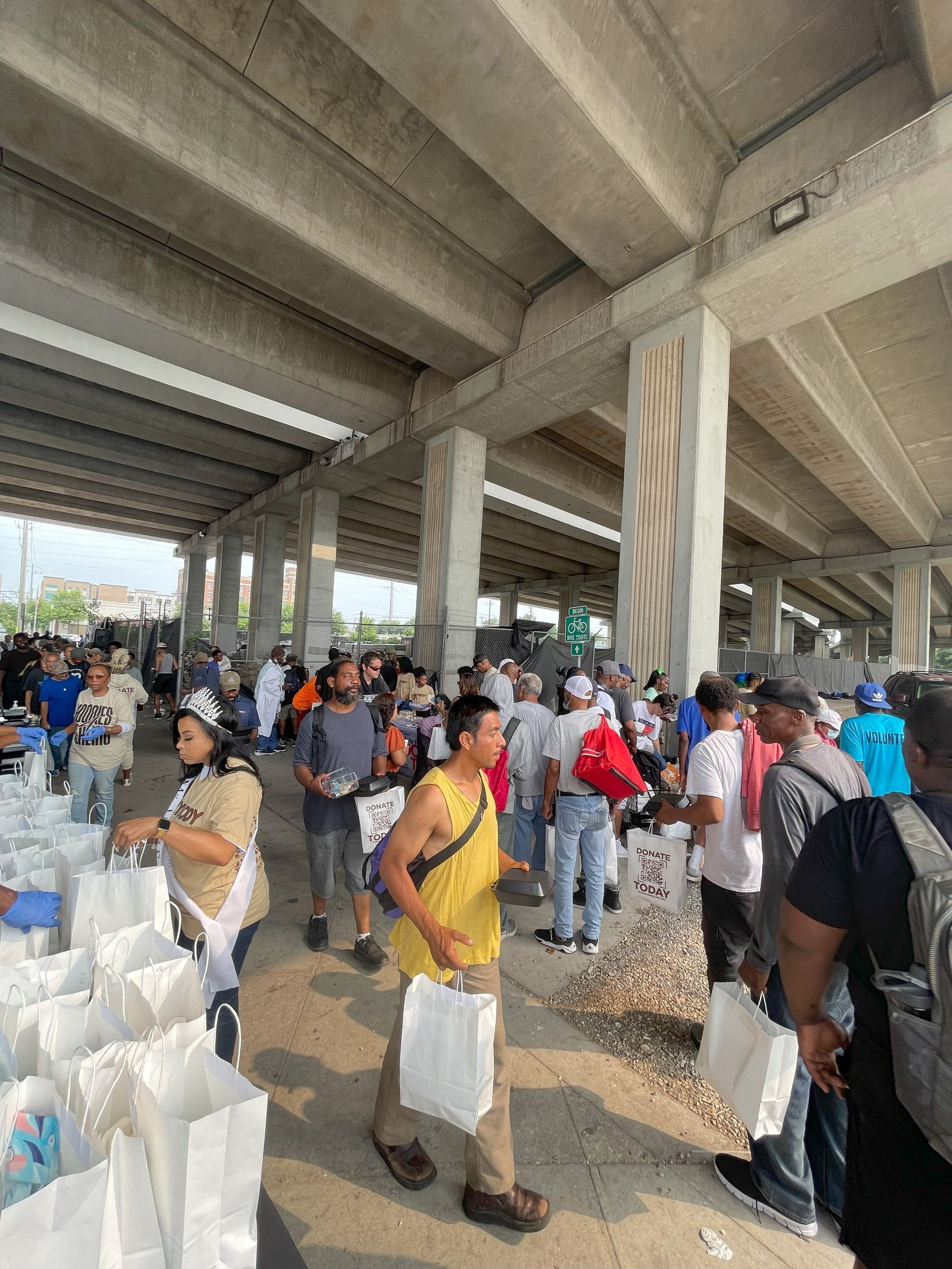 A group of people are standing under a bridge holding bags.