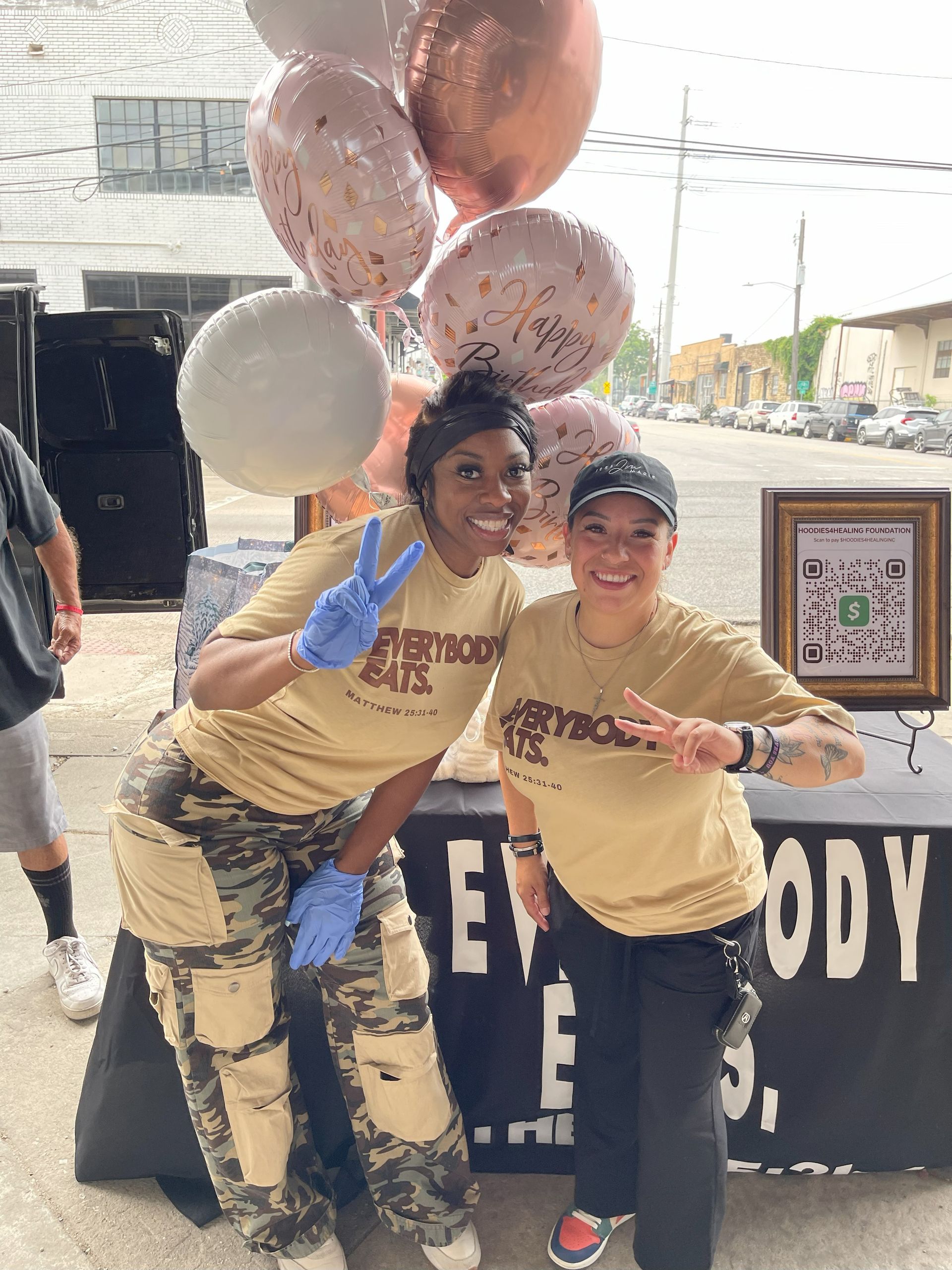 Two women are posing for a picture in front of a table with balloons.
