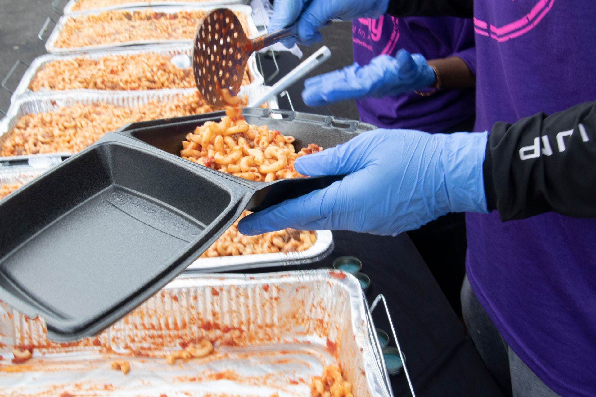 A person wearing blue gloves is holding a tray of food