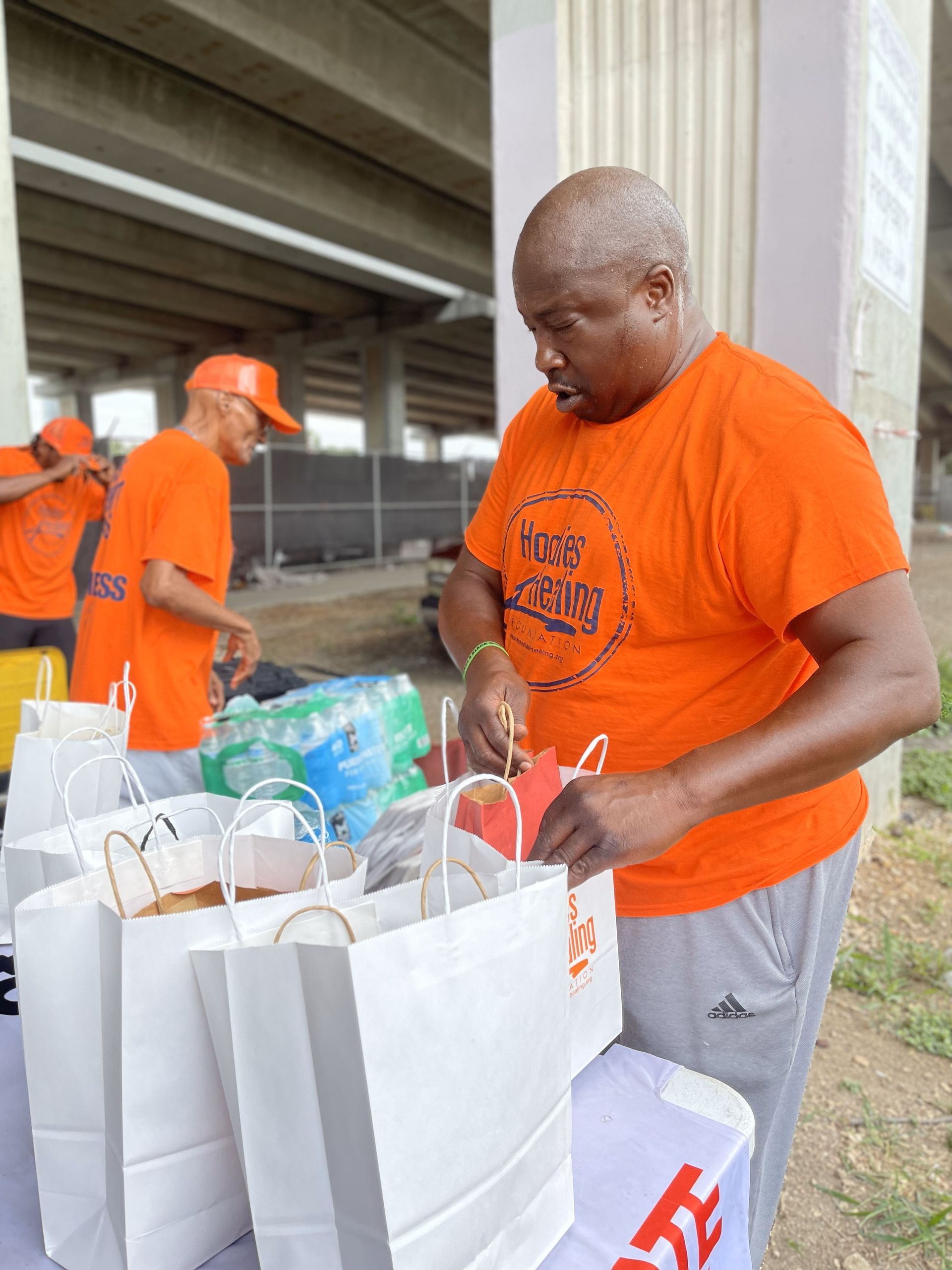 A man in an orange shirt is putting something in a bag