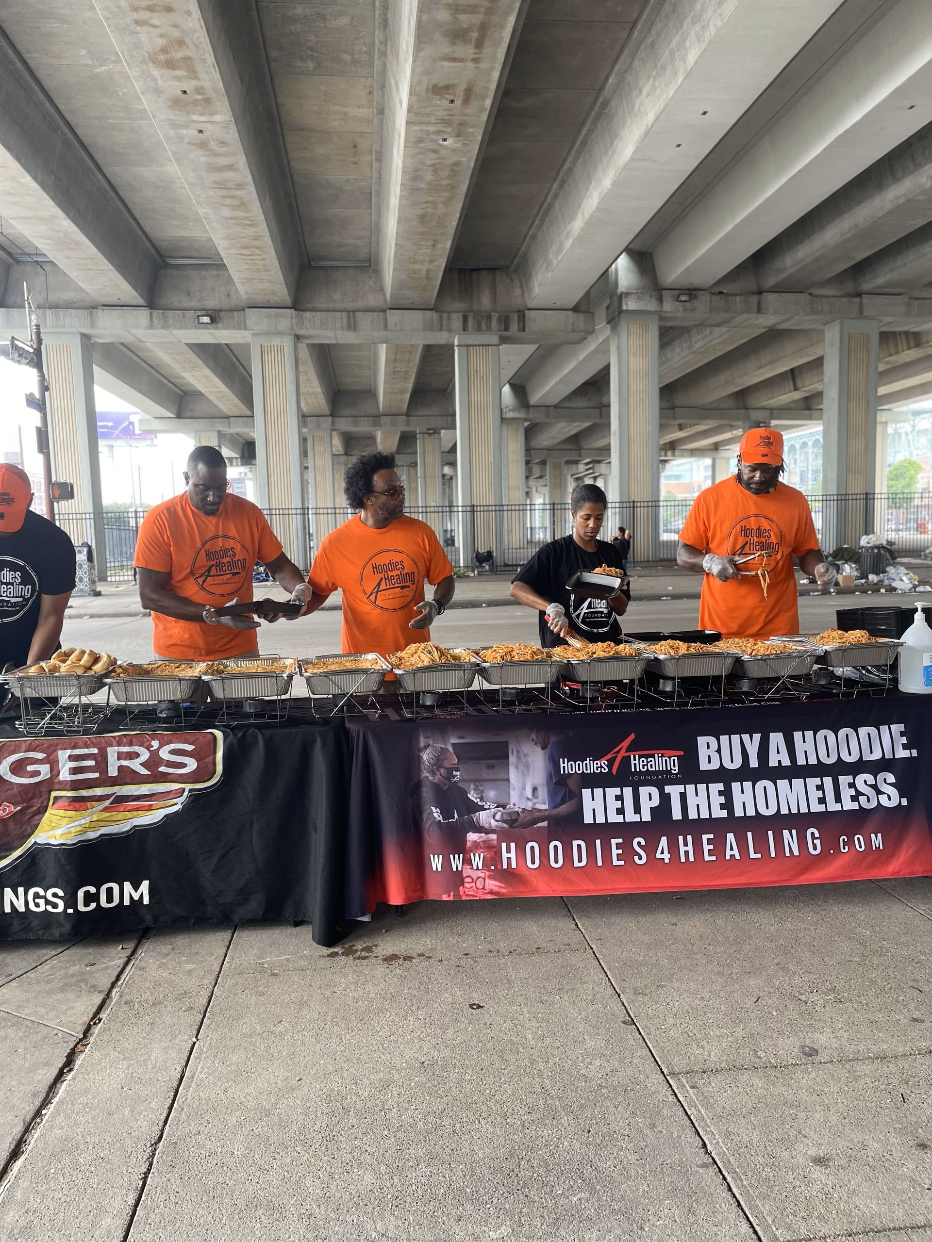 A group of people are standing around a table serving food under a bridge.