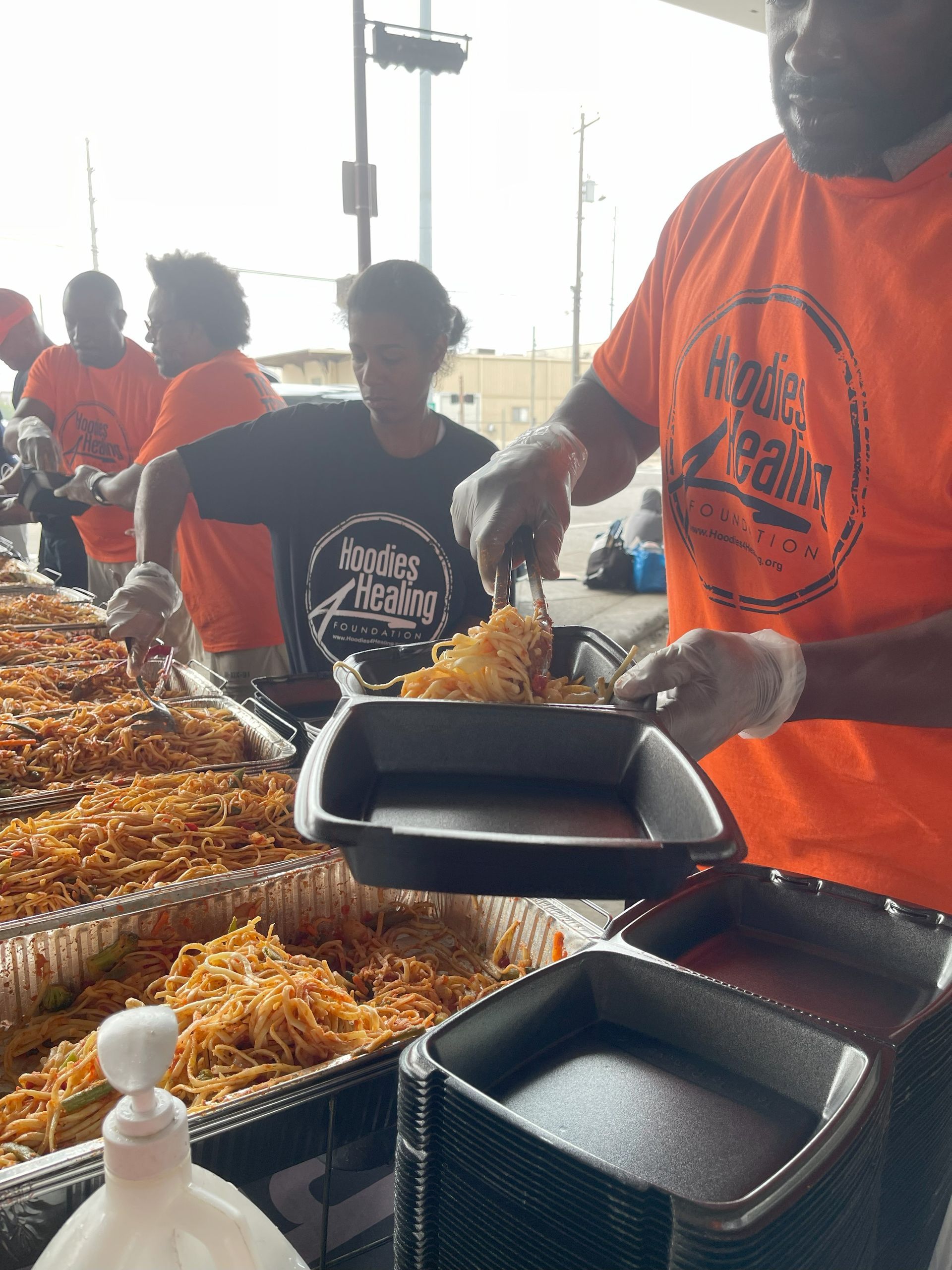 A man in an orange shirt is serving food to a group of people.