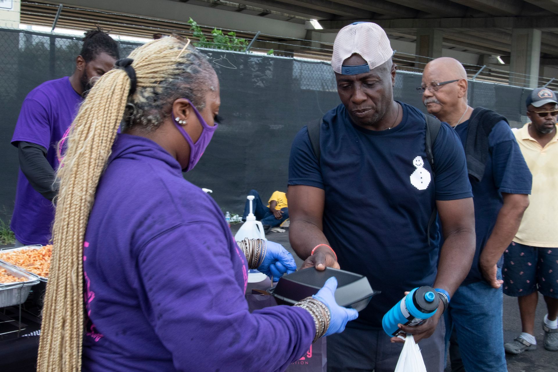 A woman wearing a mask is serving food to a man.