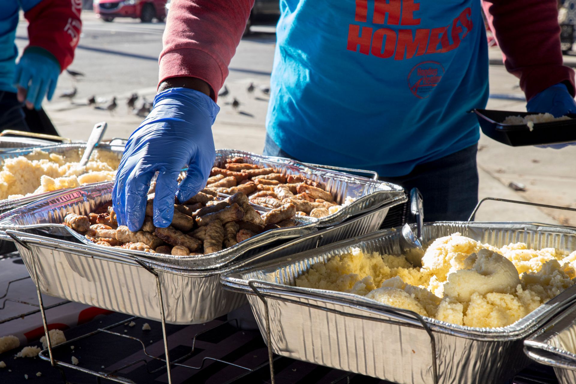 A person wearing blue gloves is reaching into a tray of food.
