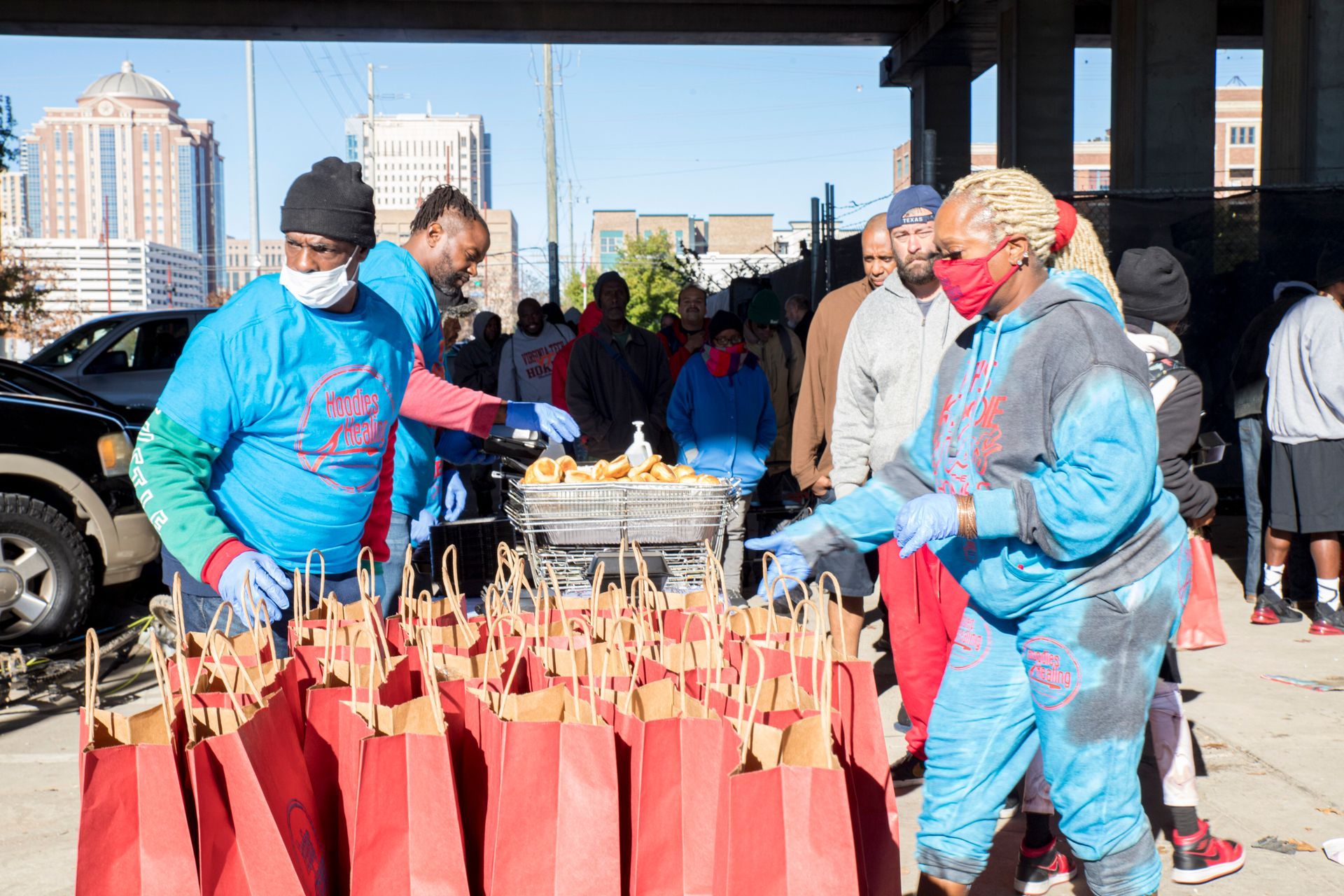 A group of people are standing around a table with bags of food.