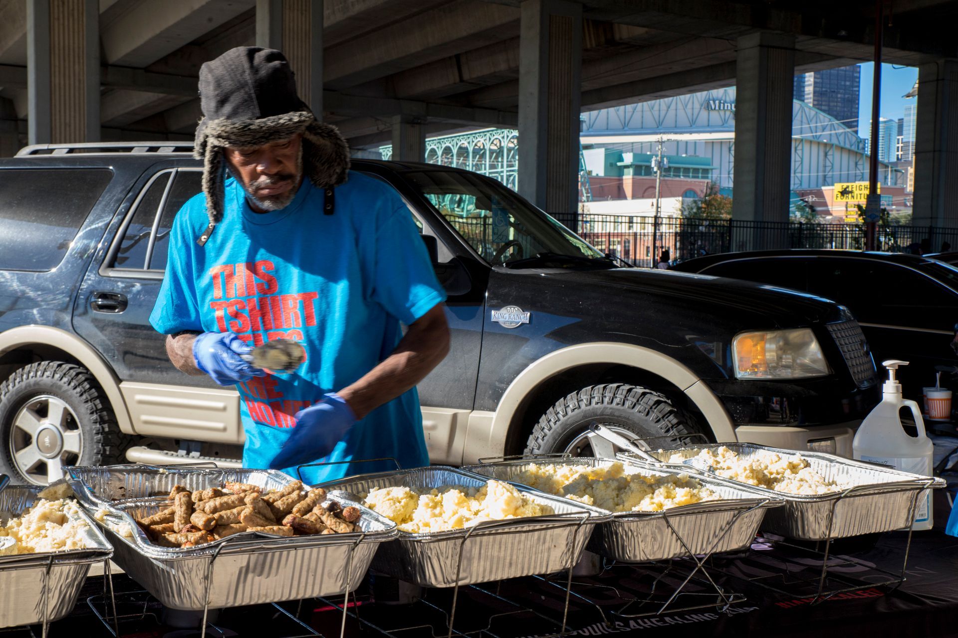 A man is preparing food in front of a car in a parking lot.