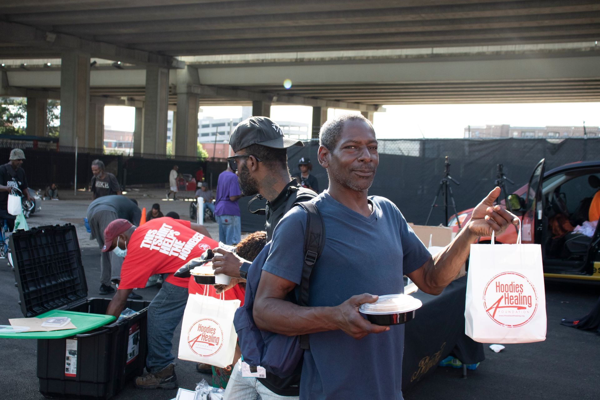 A man is standing in a parking lot holding a bowl of food and a bag.