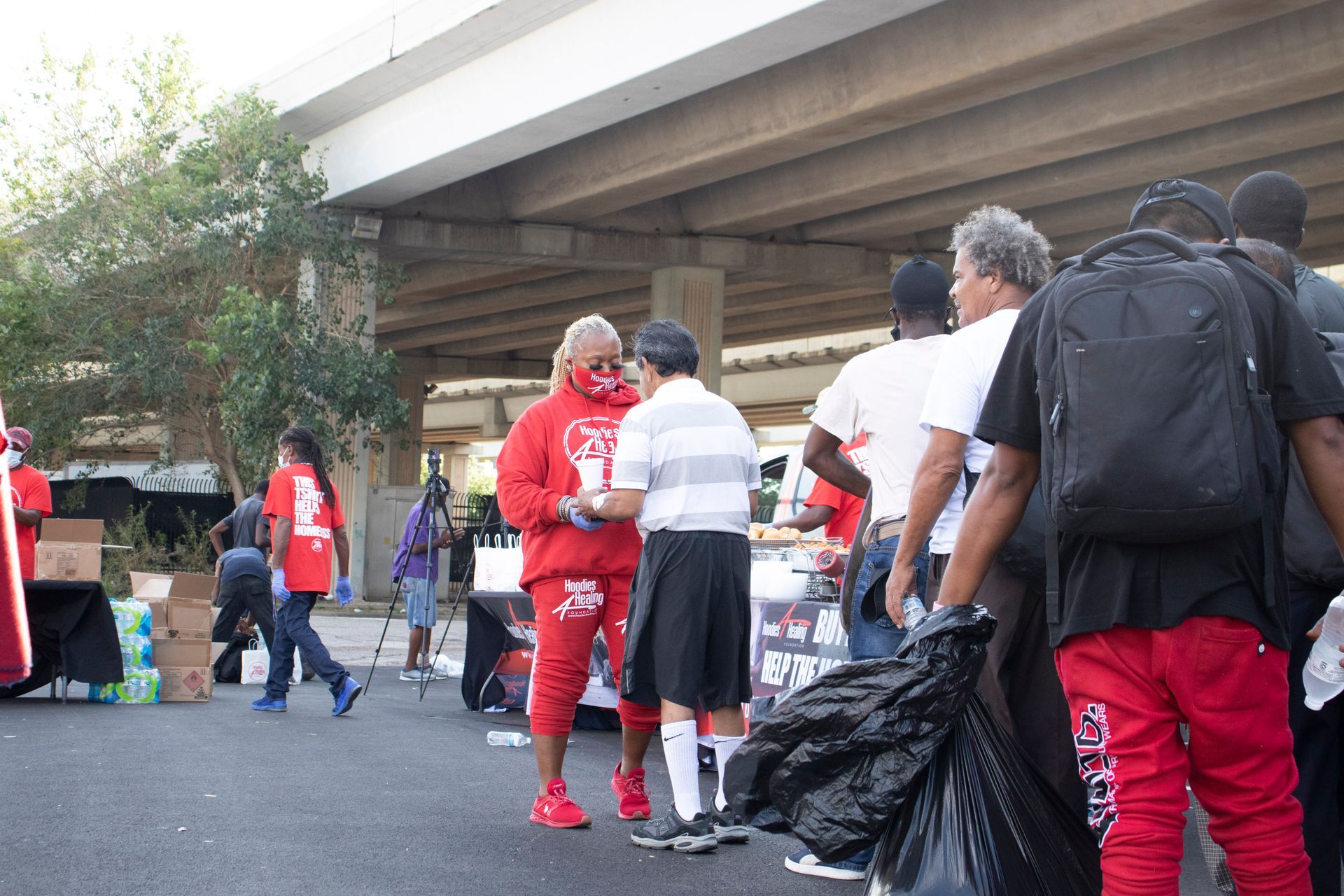 A group of people are standing in a parking lot under a bridge.