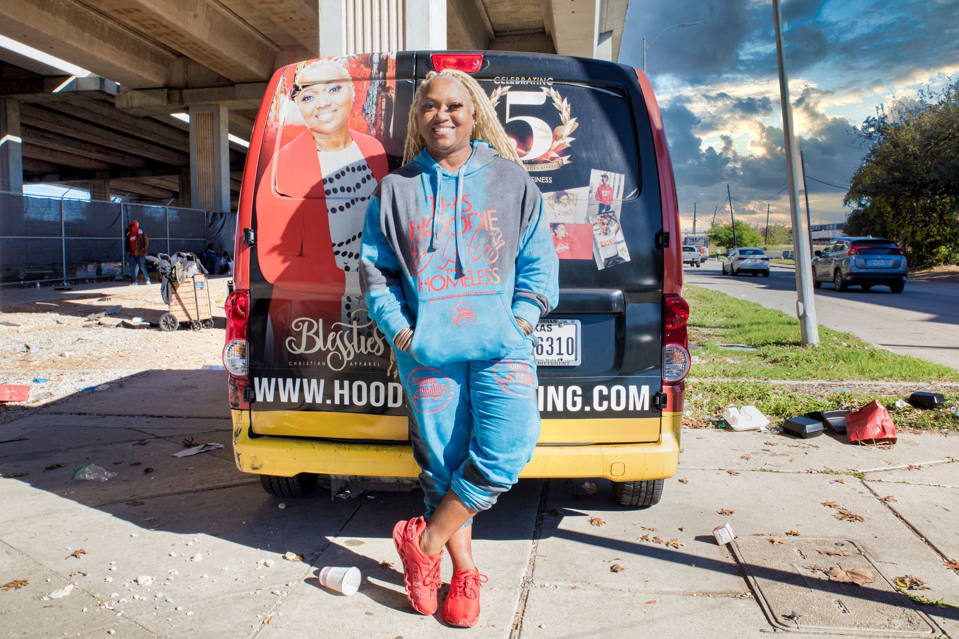 A woman in a blue hoodie is standing in front of a van.