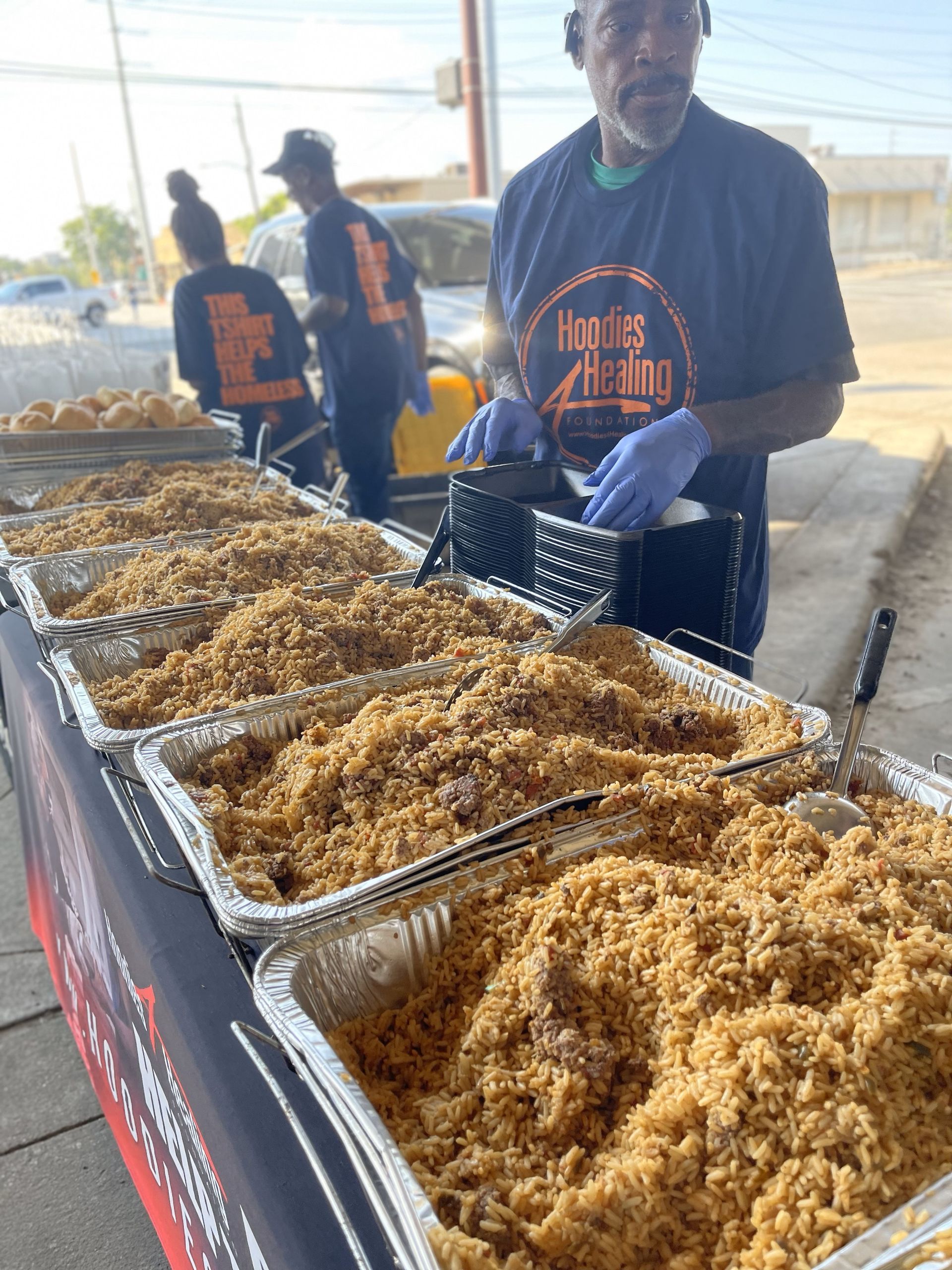 A man is standing behind a table filled with trays of food.