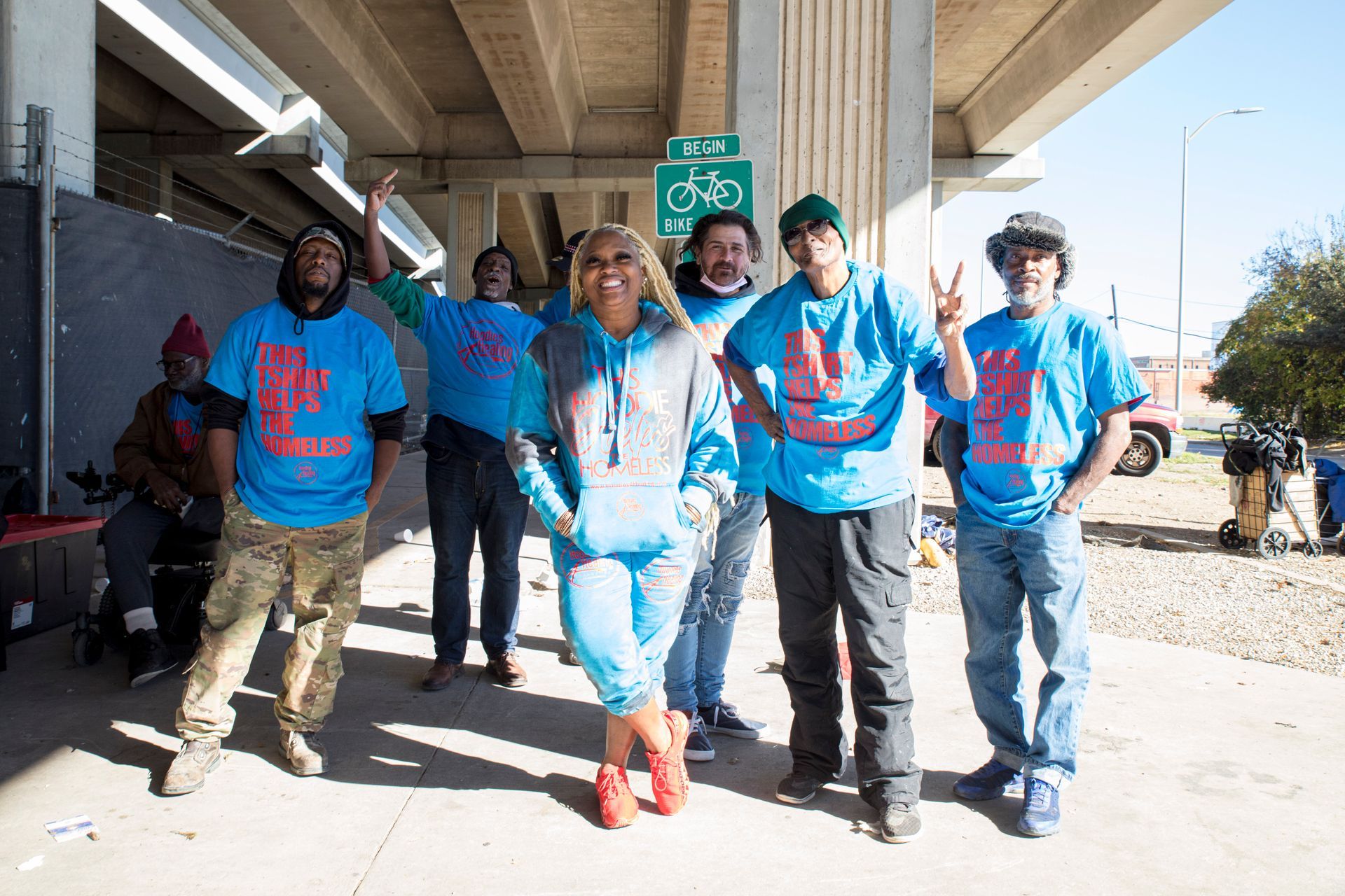 A group of people wearing blue shirts are posing for a picture under a bridge.
