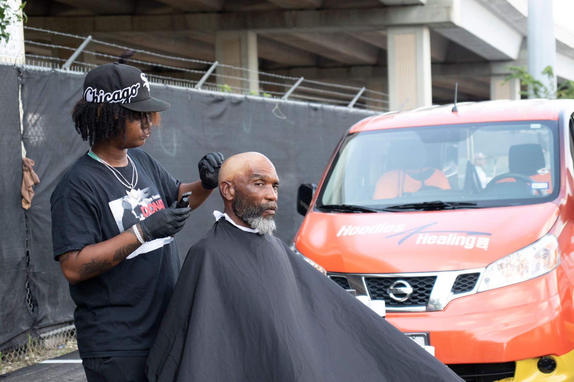 A man is getting his hair cut in front of a nissan van.