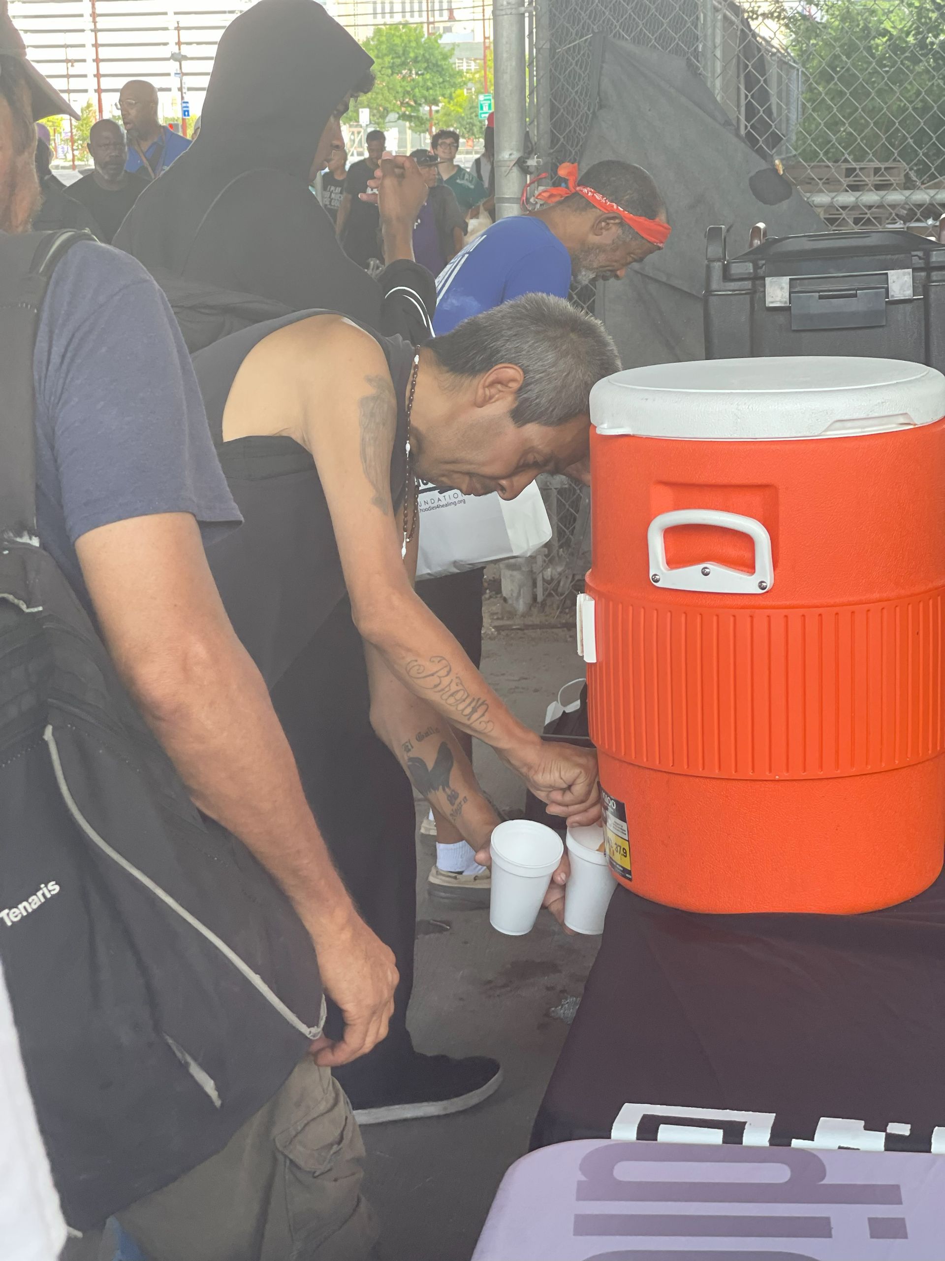 A group of people are gathered around an orange cooler with the letter d on it