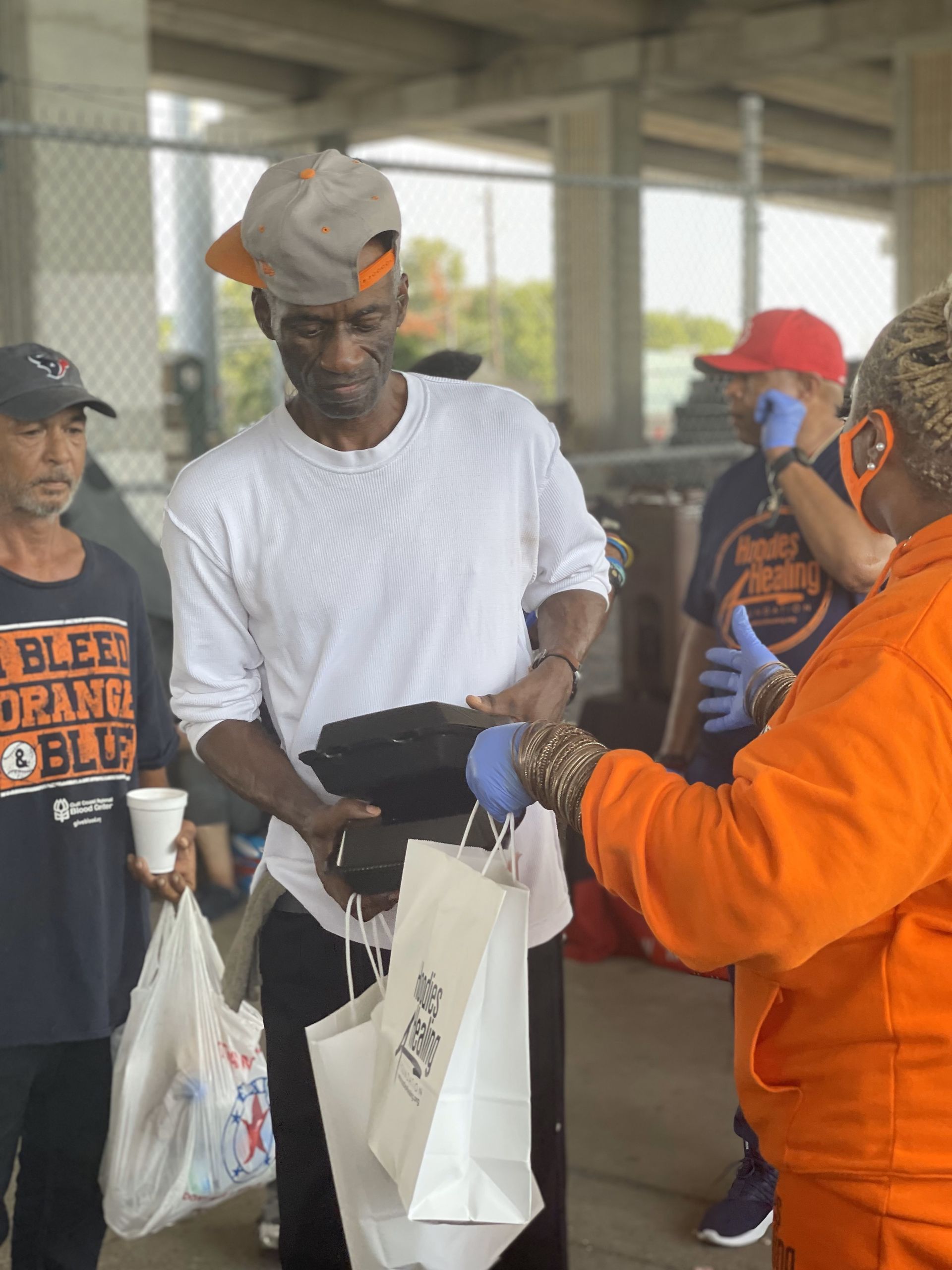 A woman in an orange hoodie is giving a man a bag of food.