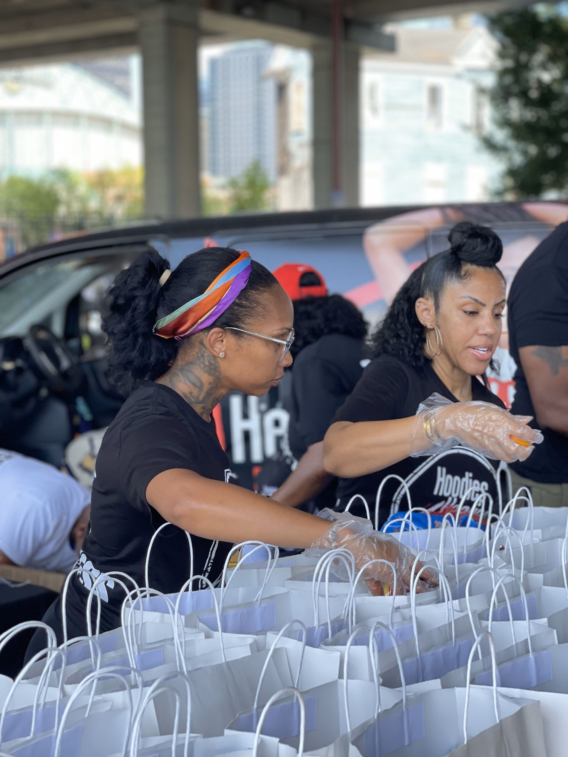 Two women are standing next to each other in front of a car filled with bags.