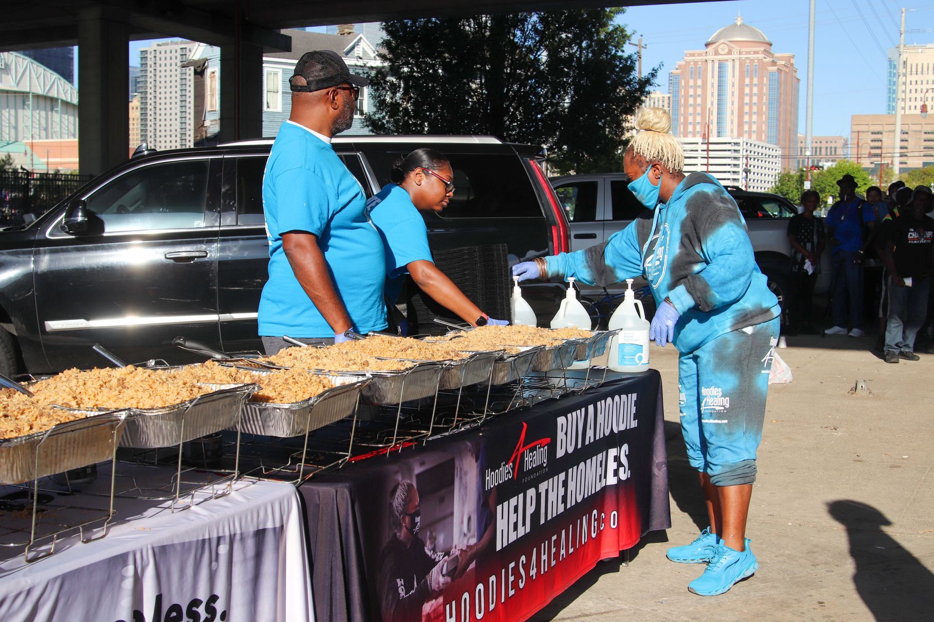 A group of people standing around a table with trays of food on it.
