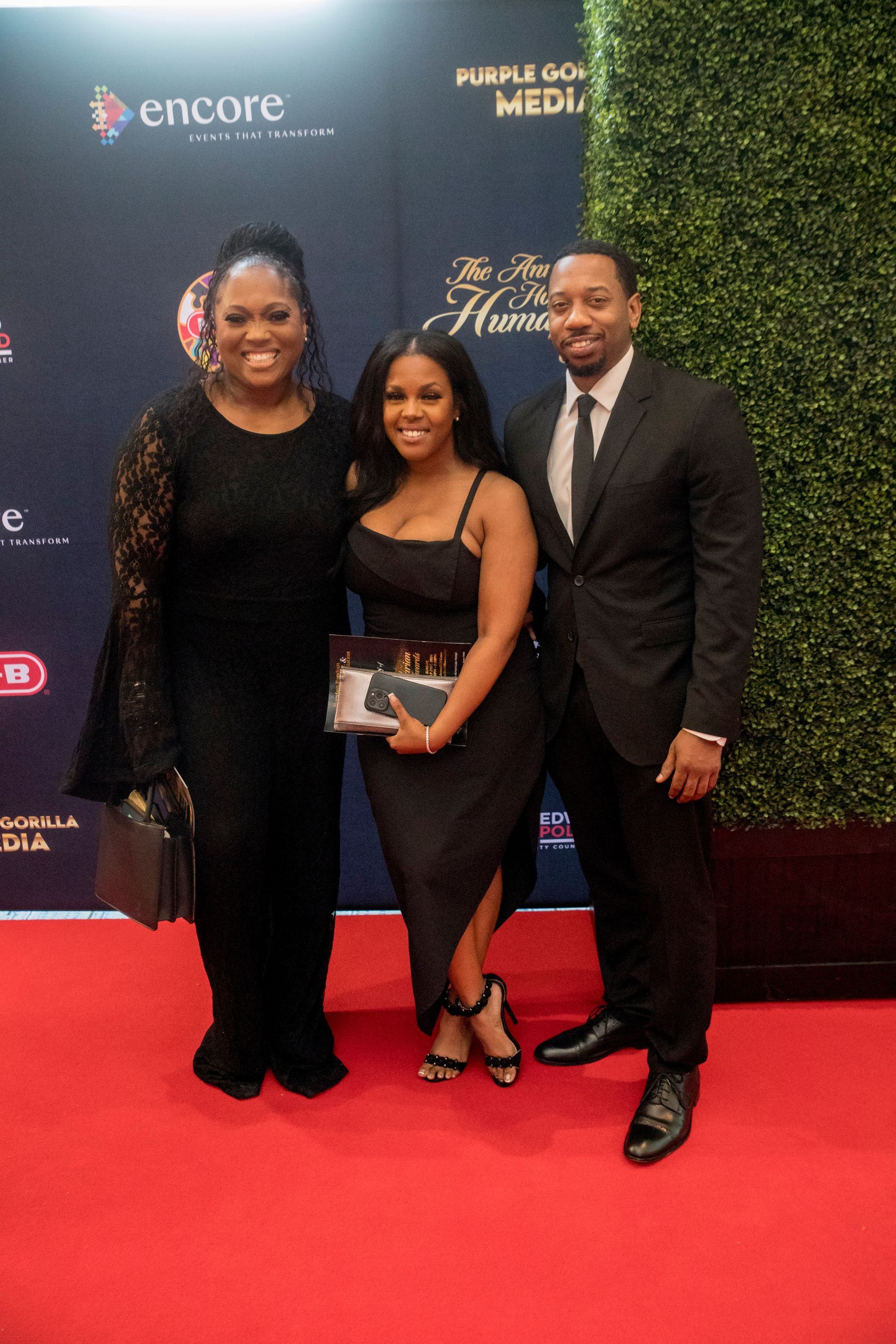 A man and two women are posing for a picture on a red carpet.