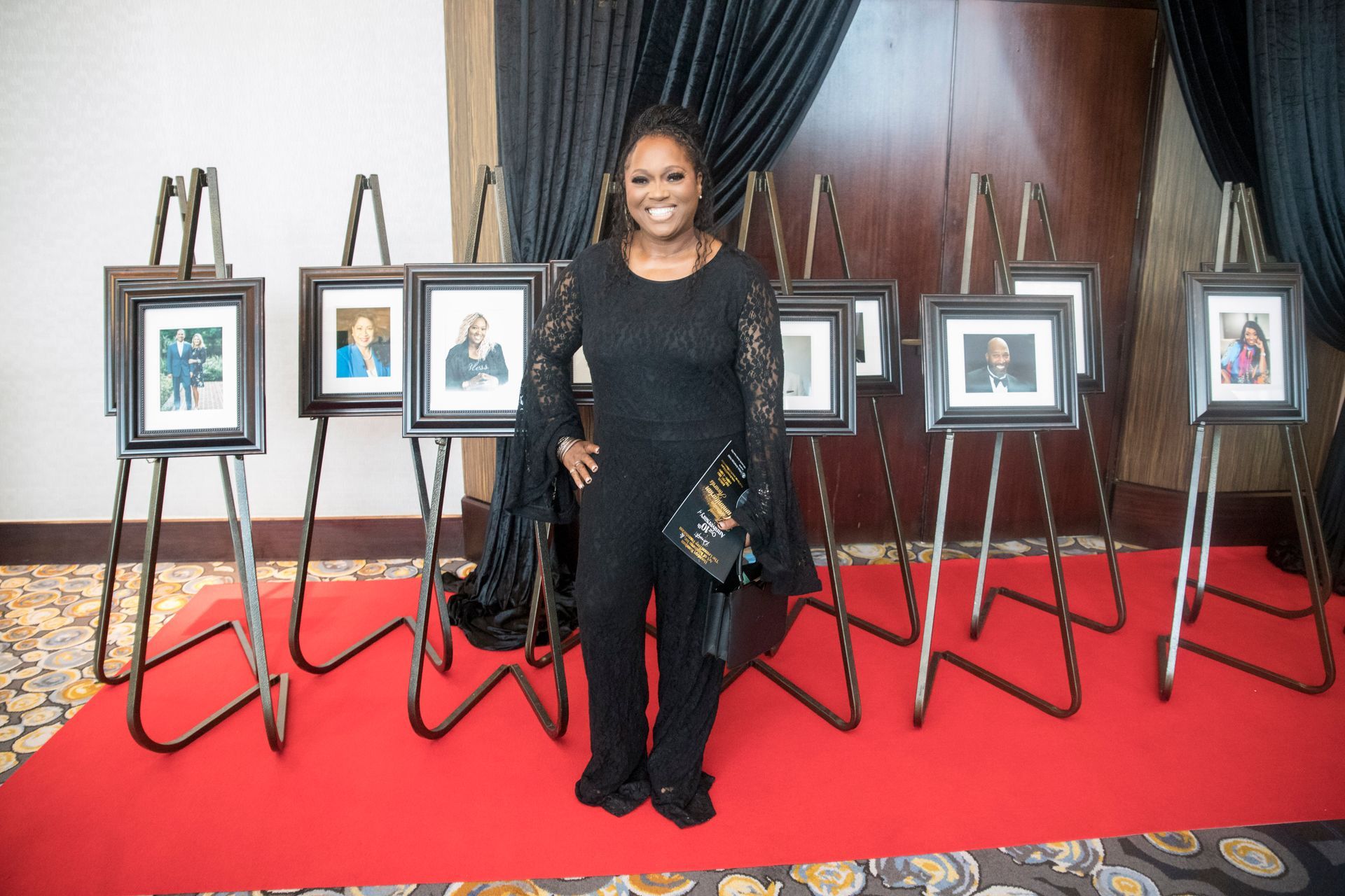 A woman in a black dress is standing in front of a row of easels with pictures on them.