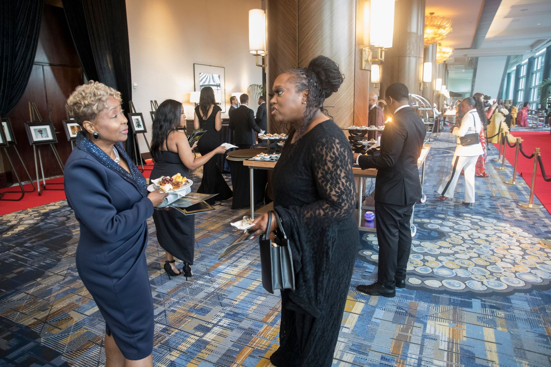 A group of women are standing in a room talking to each other.