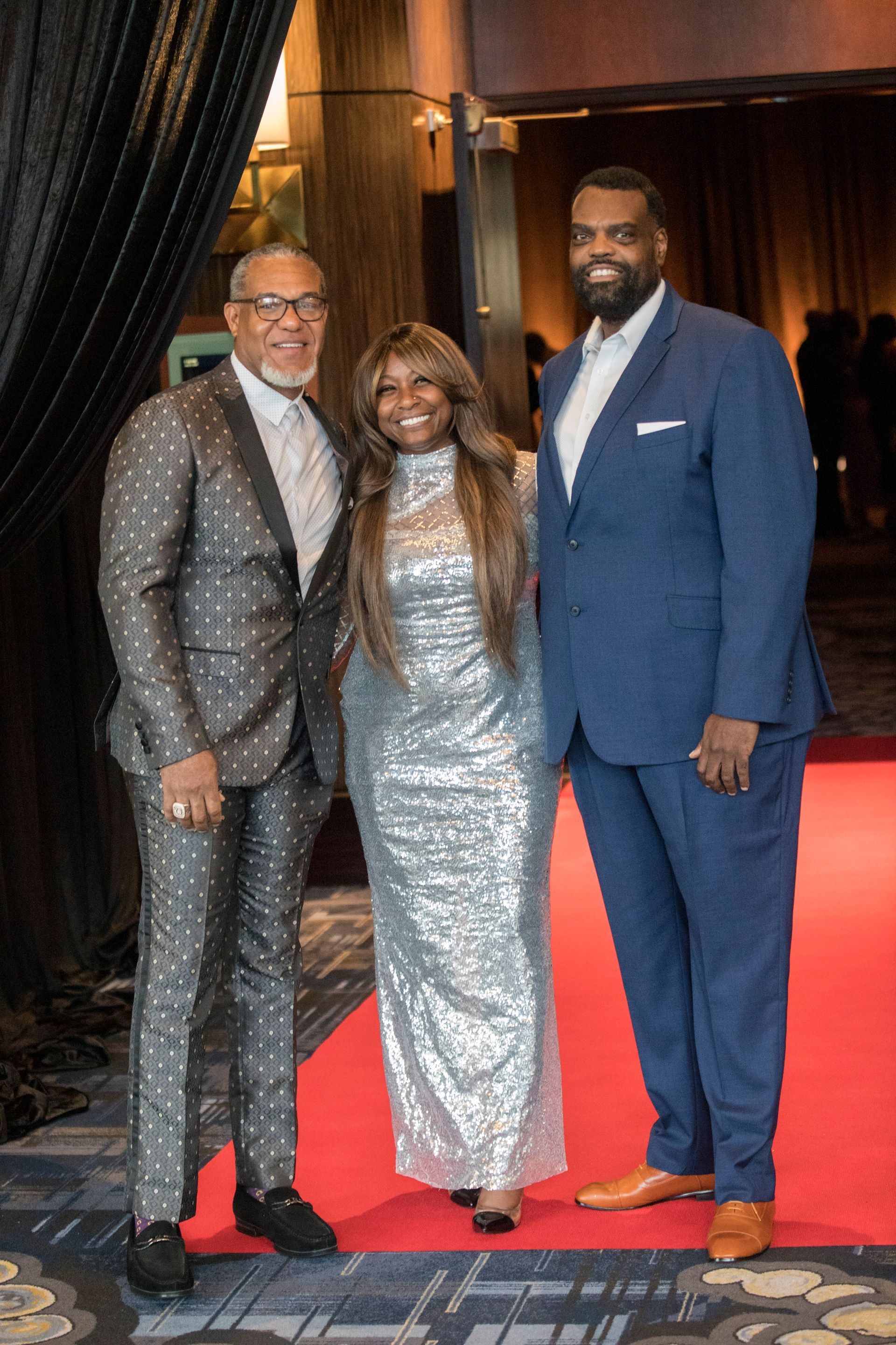 Three people are posing for a picture on a red carpet.