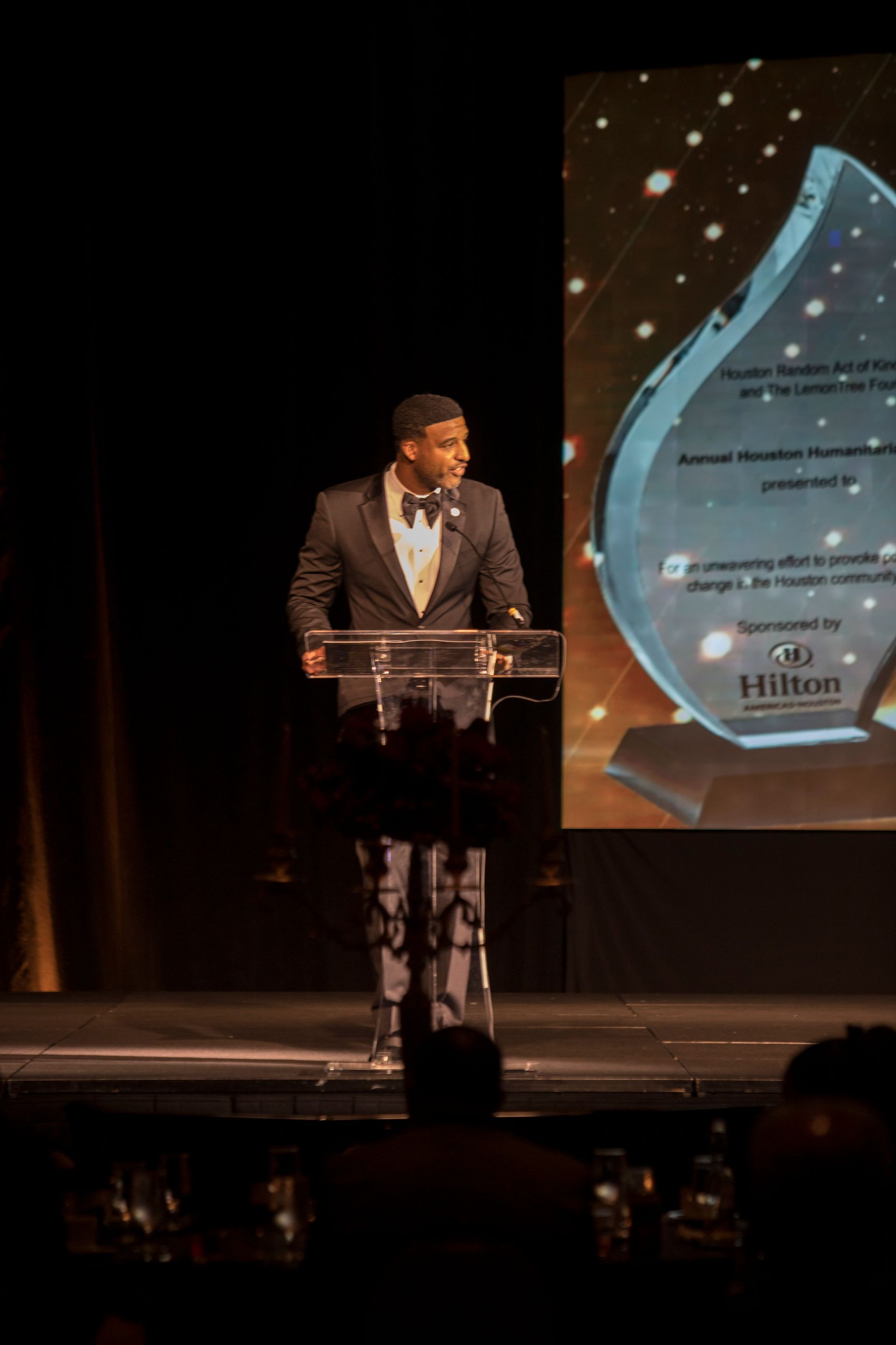 A man in a tuxedo is standing at a podium giving a speech.