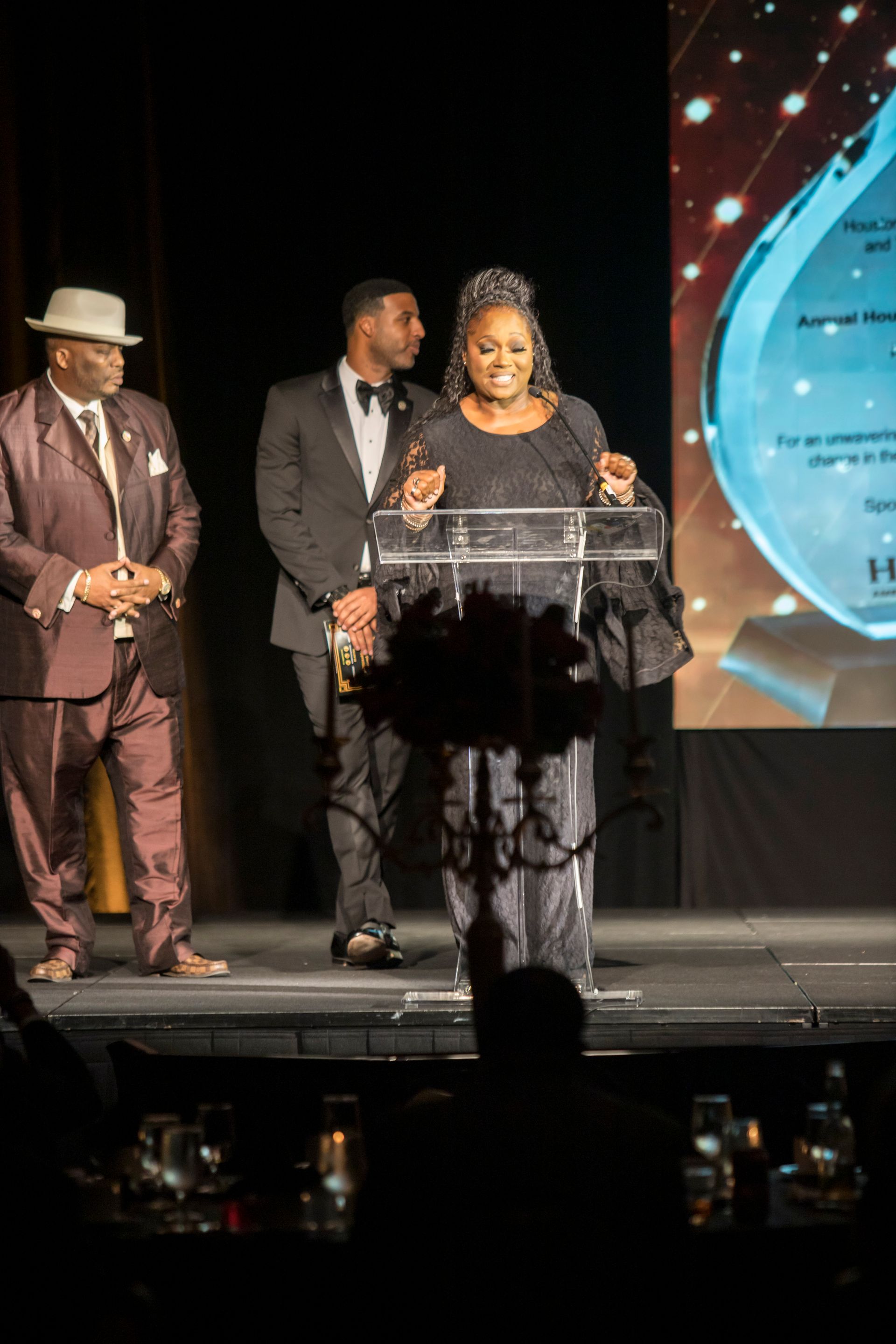 A woman is standing at a podium giving a speech while two men stand behind her.