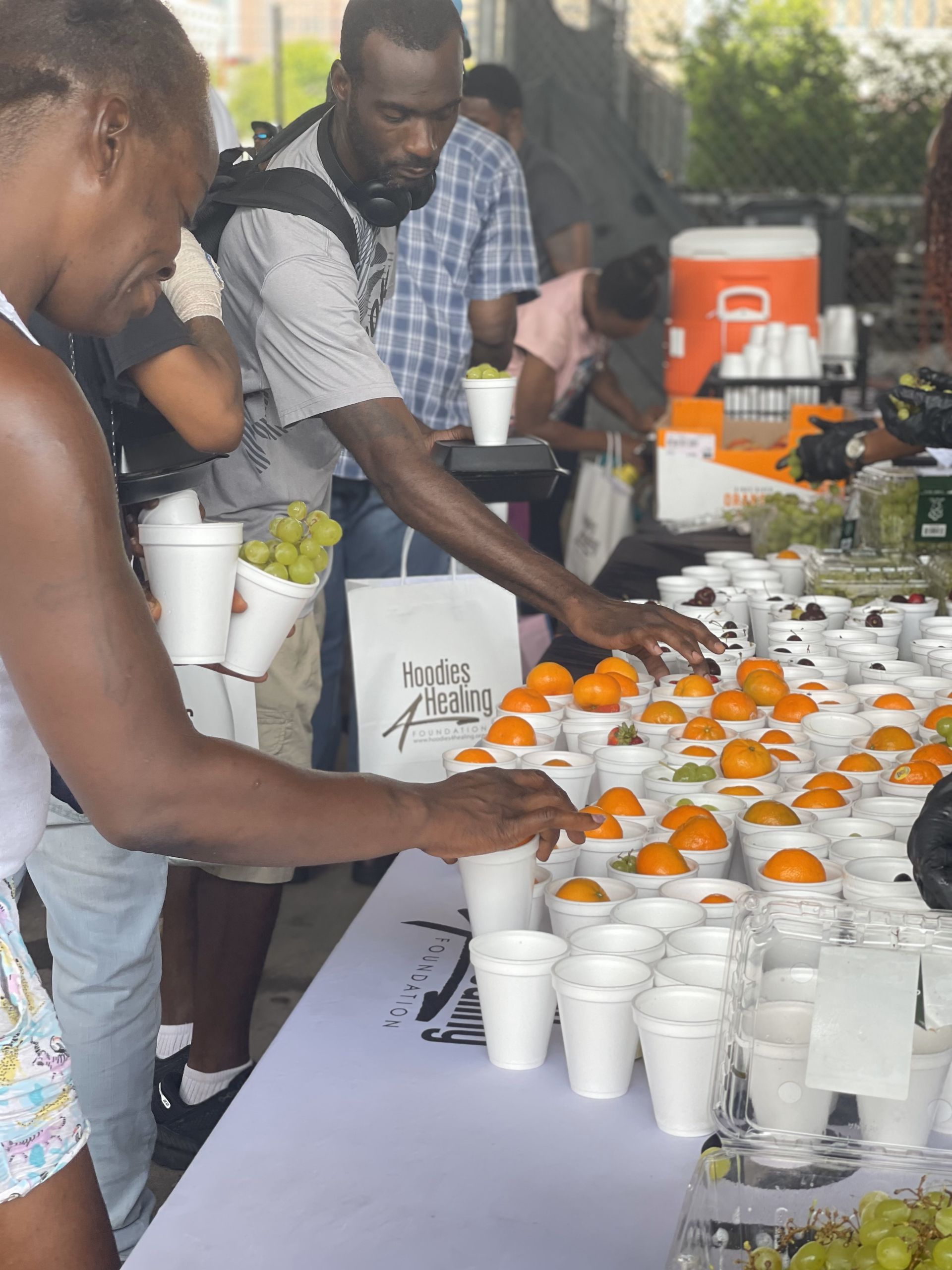 A group of people are standing around a table filled with cups of fruit