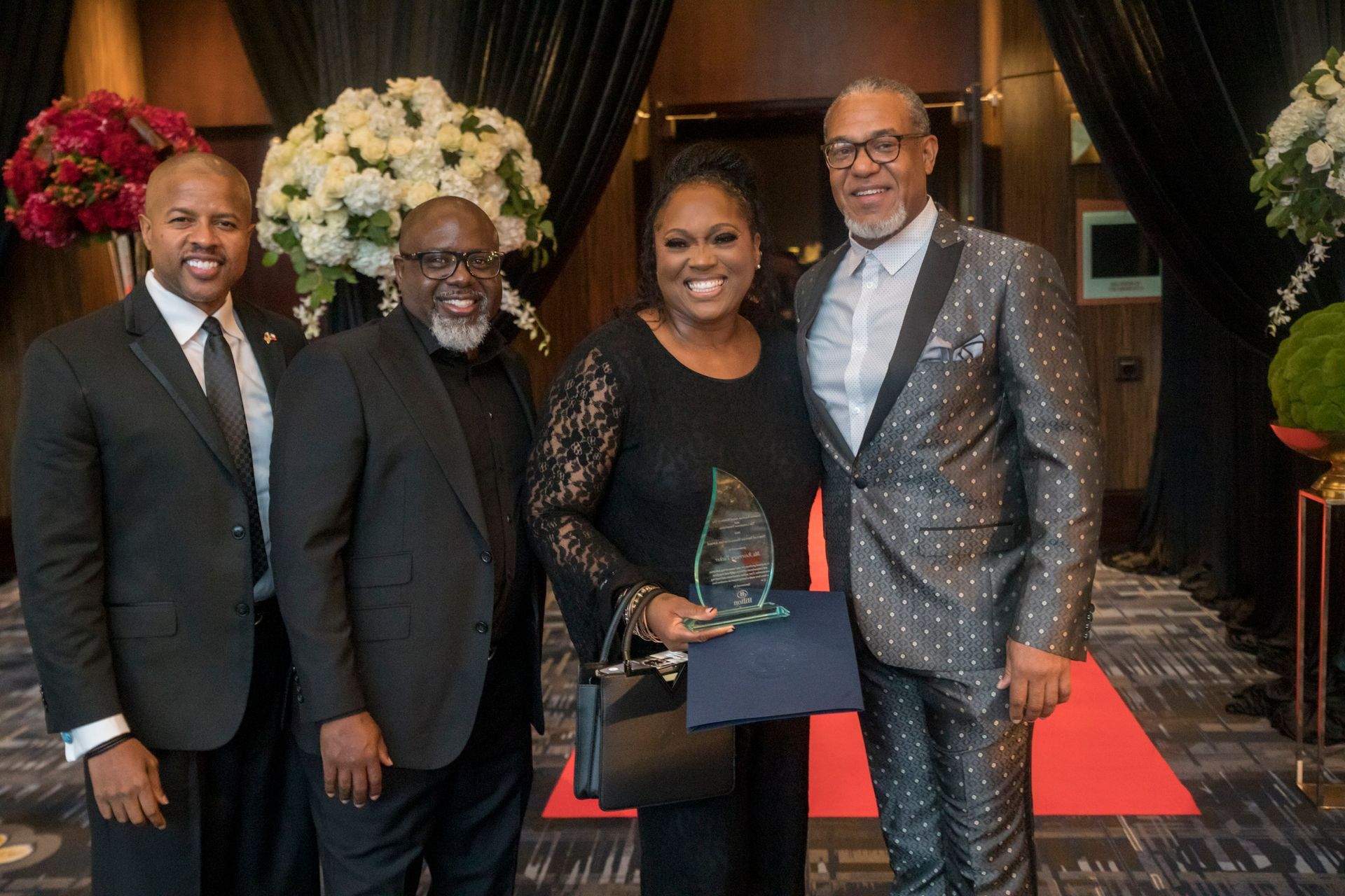 A woman is holding an award while standing next to two men in suits.