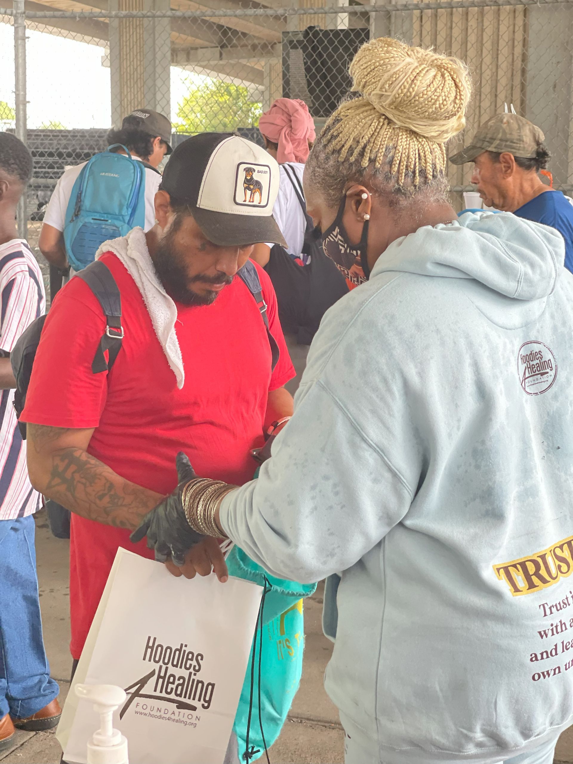 A man in a red shirt is talking to a woman in a blue sweatshirt with the word trust on it