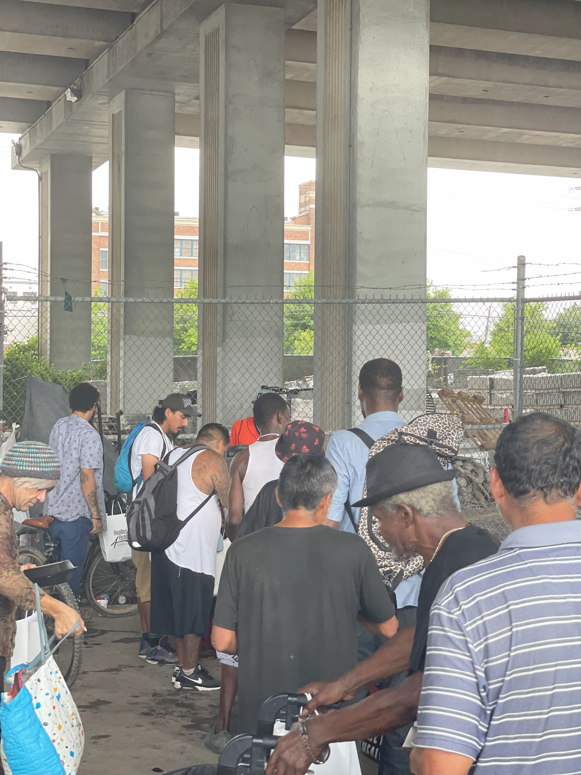 A group of people are standing in a line under a bridge.