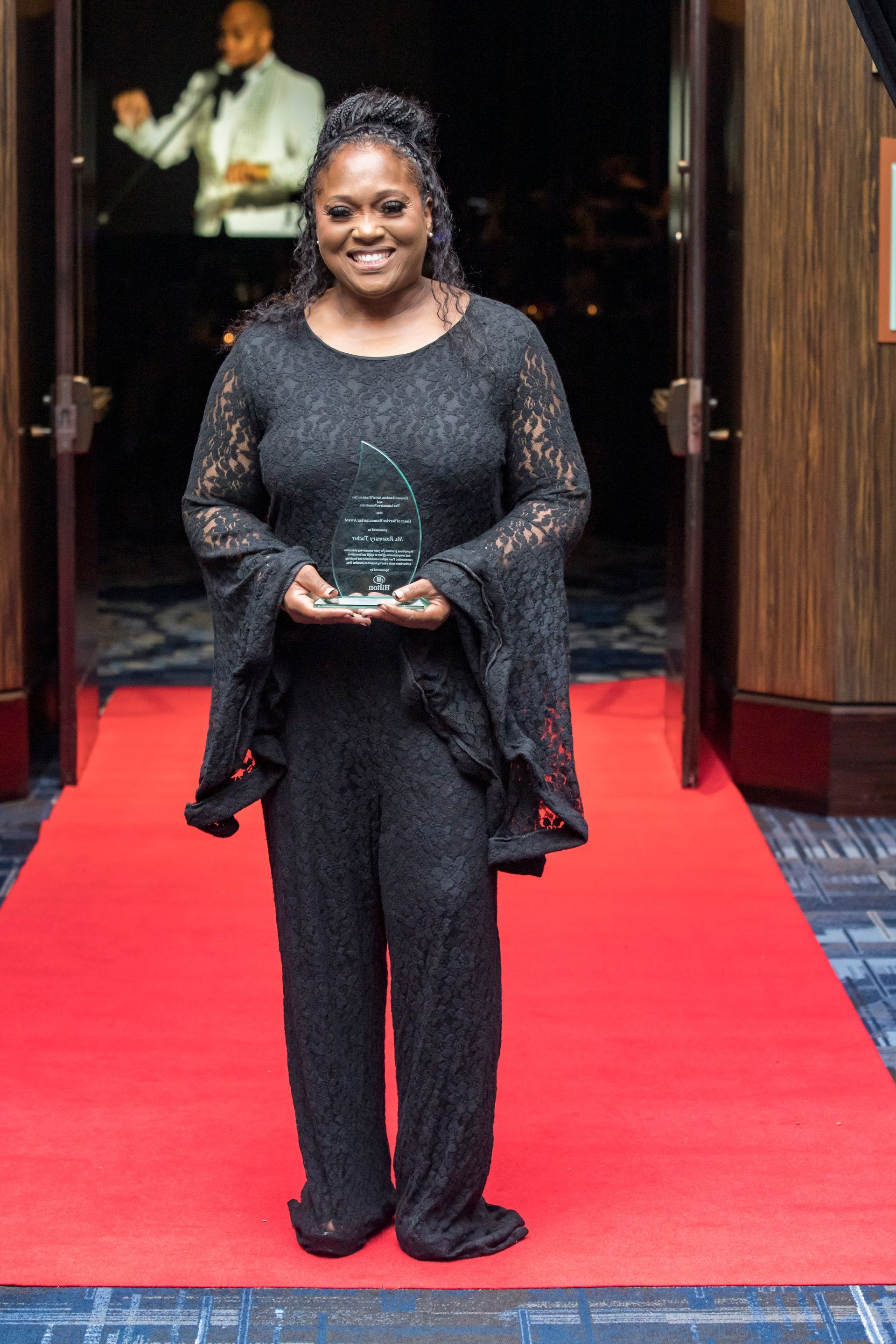 A woman is standing on a red carpet holding an award.