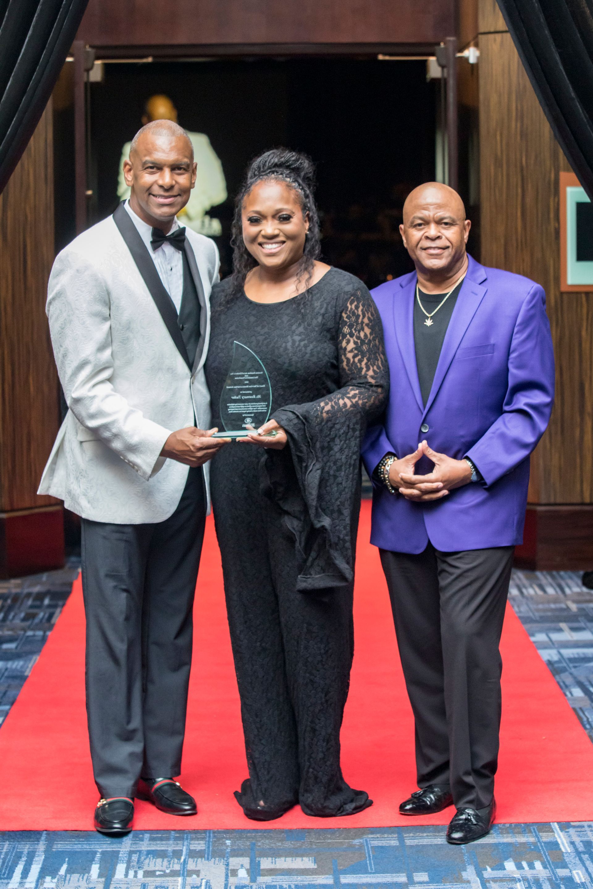 Two men and a woman are posing for a picture on a red carpet.