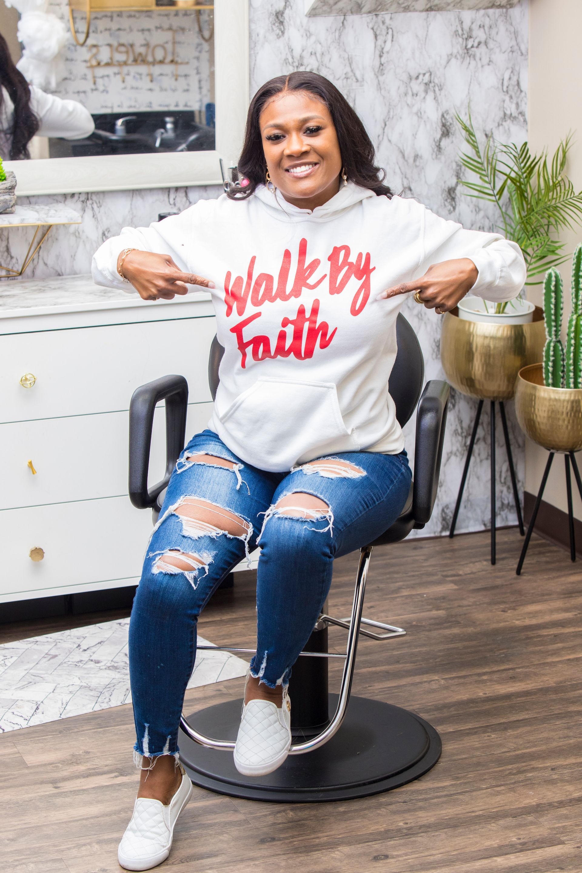 A woman is sitting in a chair wearing a hoodie that says `` walk by faith ''.