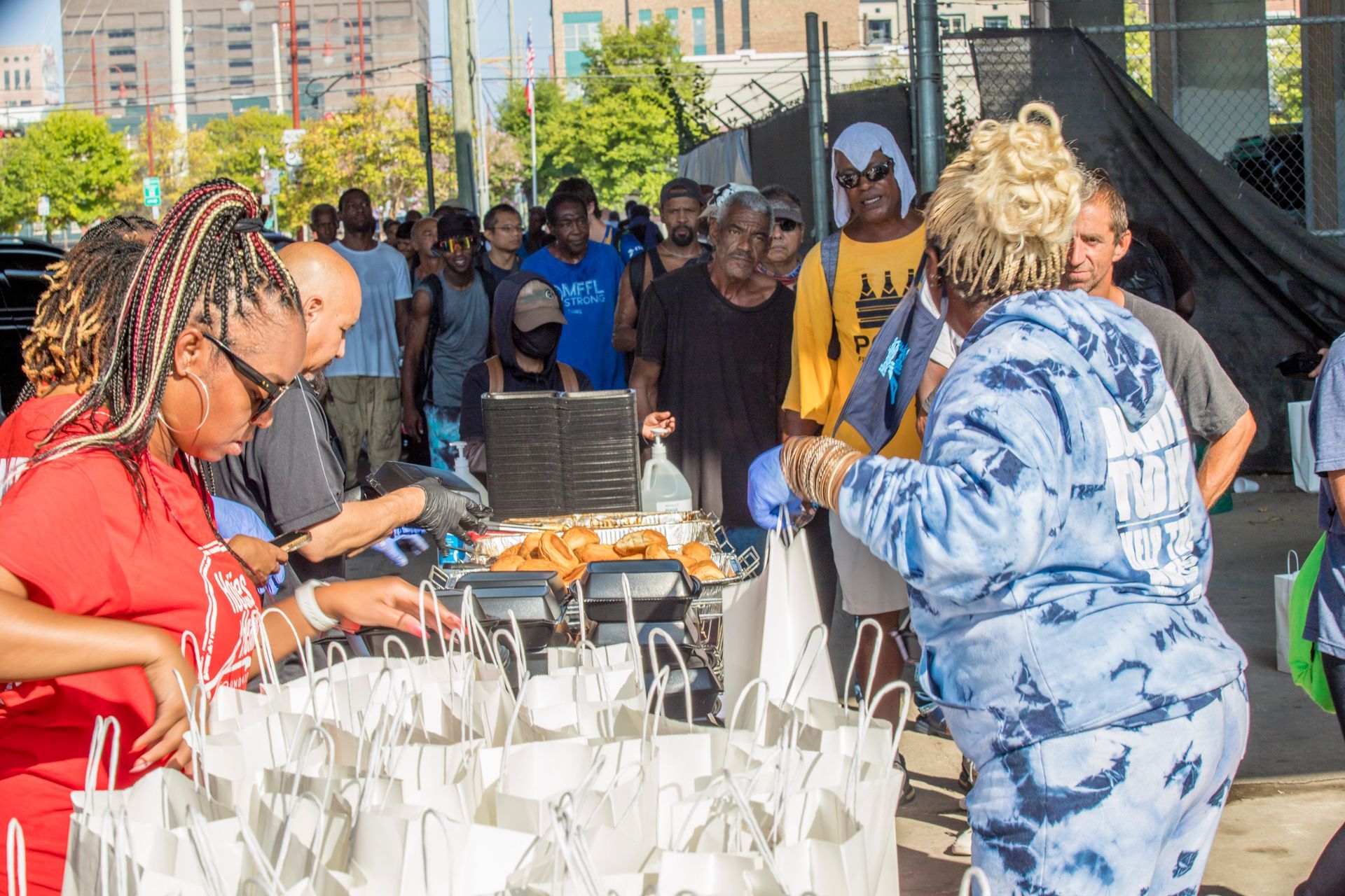 A group of people are standing around a table with bags of food.