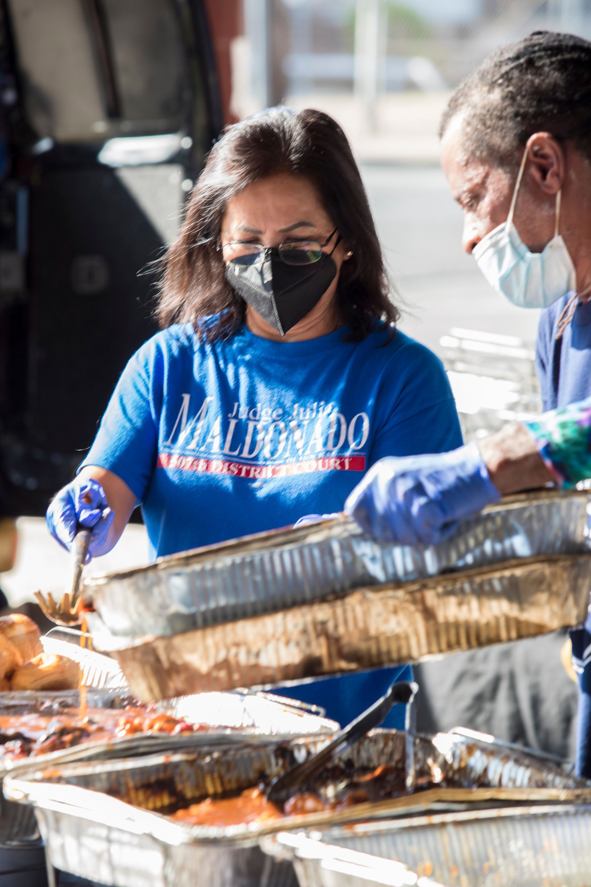 A woman wearing a mask is serving food to a man wearing a mask.