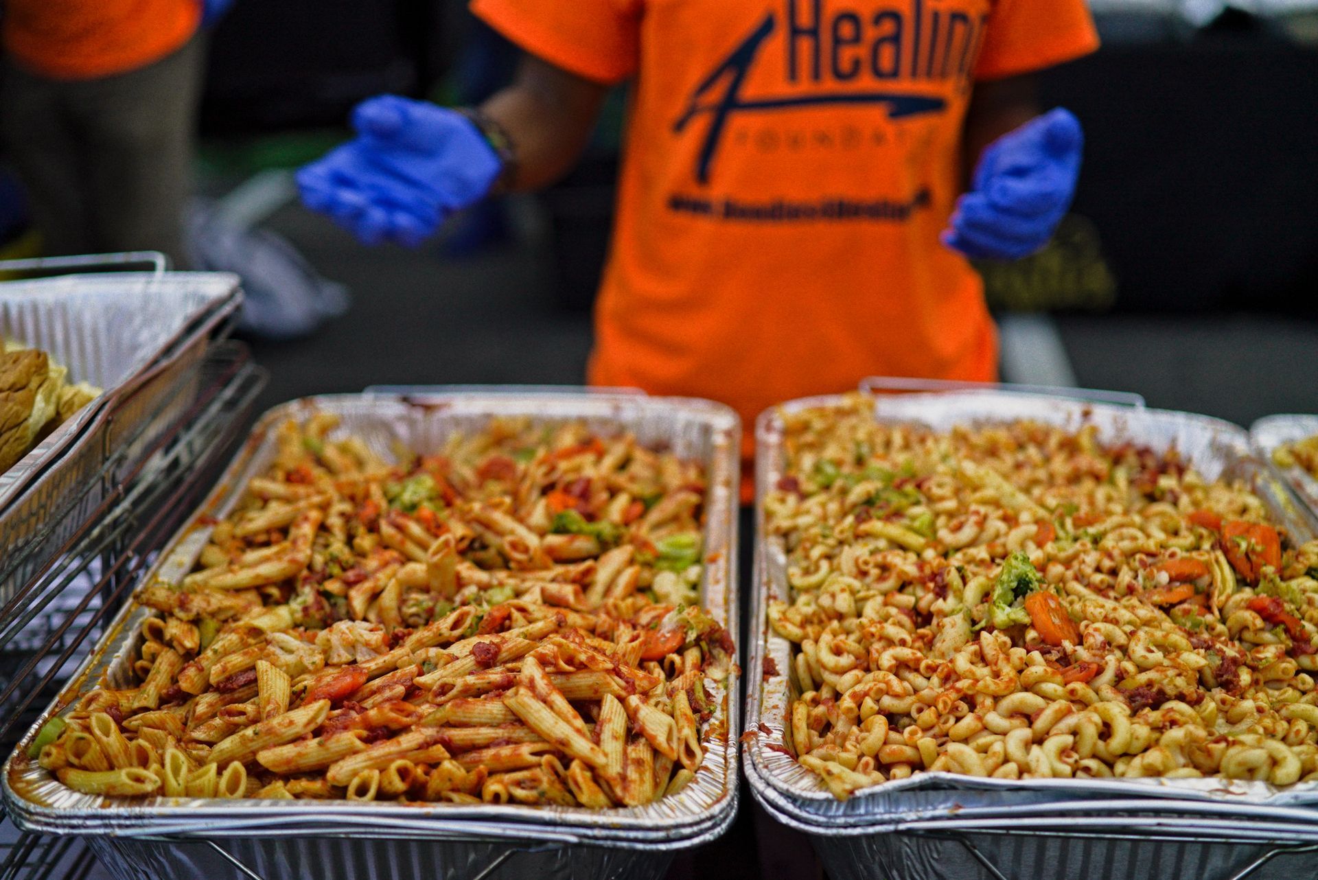 A person in an orange shirt is standing in front of a tray of food.