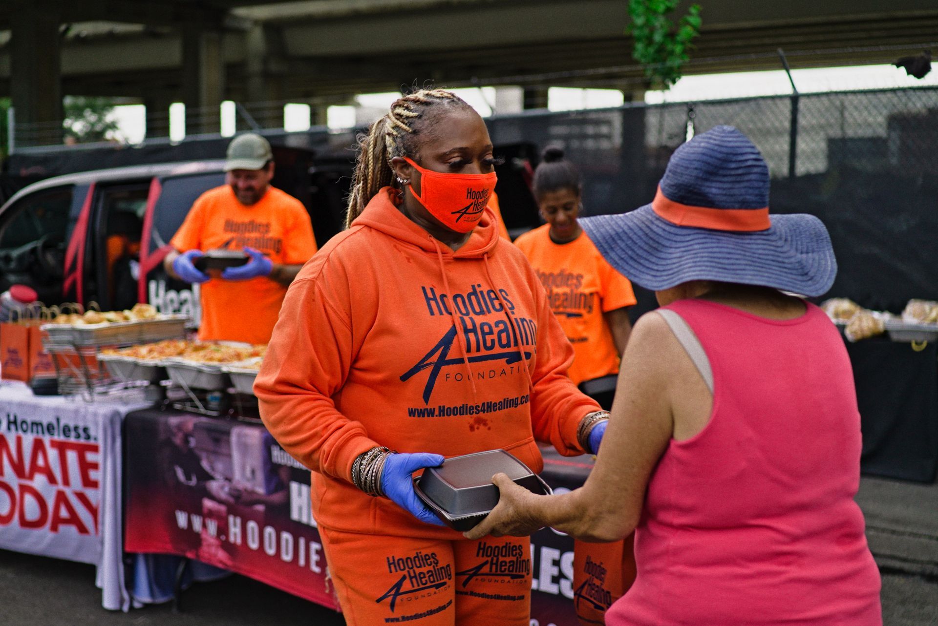 A woman wearing a mask is giving a box of food to another woman.