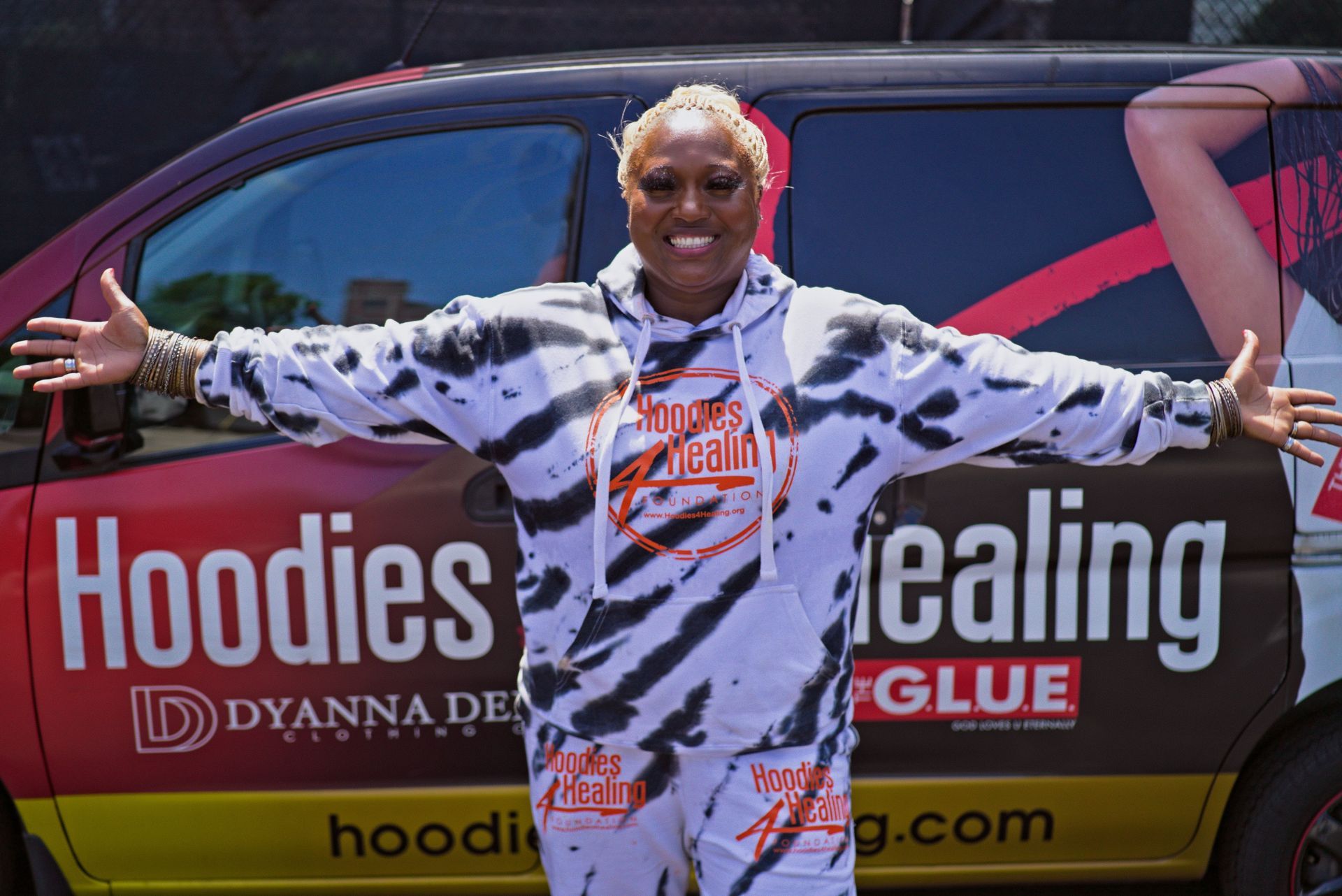 A woman is standing in front of a van that says hoodies healing glue.