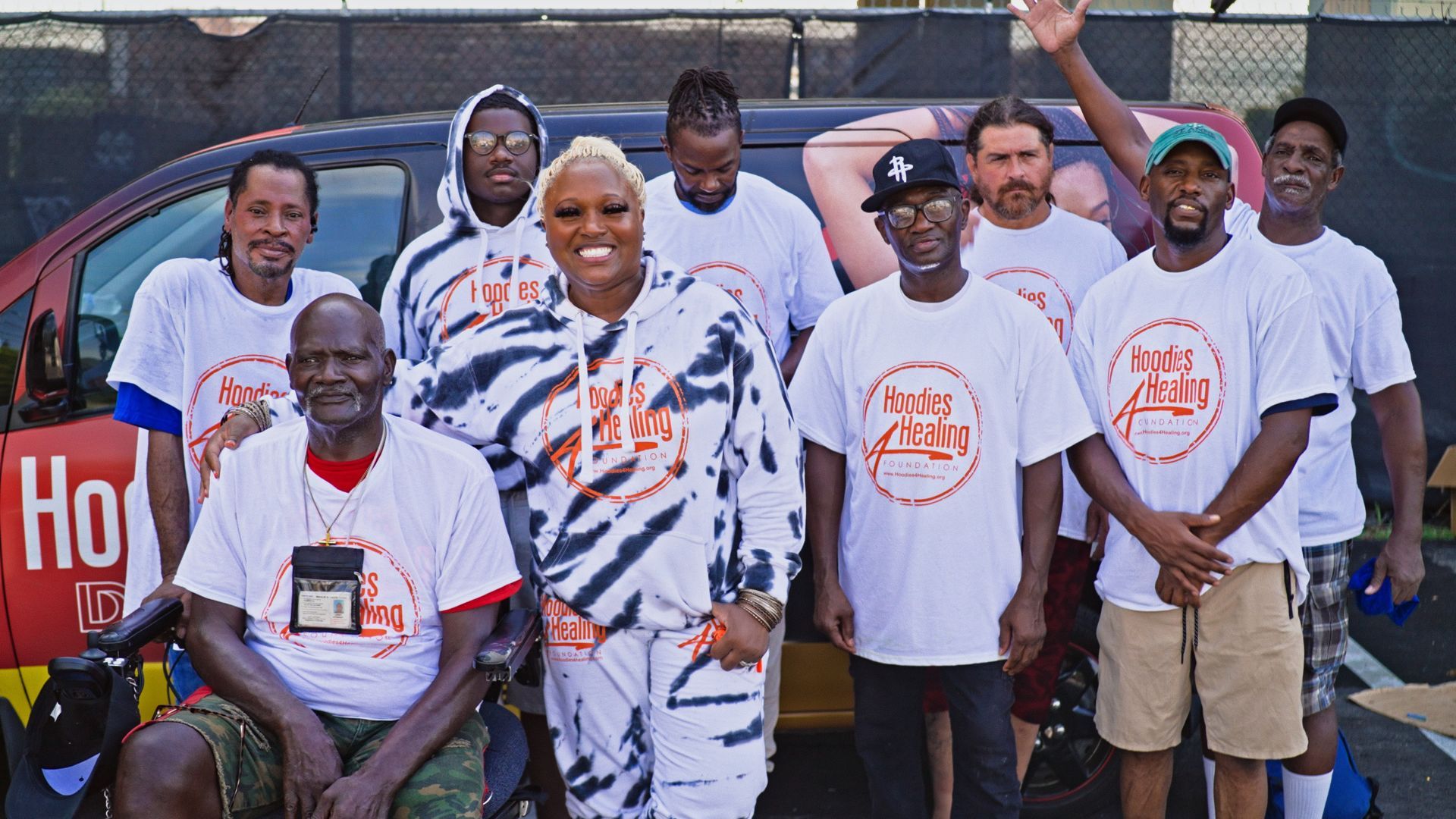 A group of people are posing for a picture in front of a van that says ho on it.