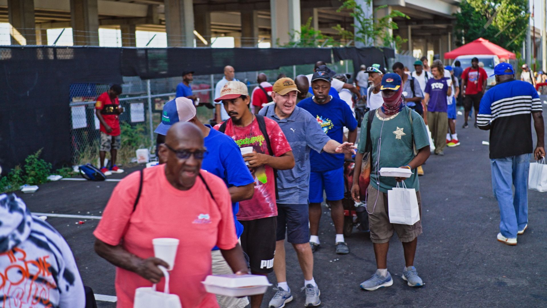 A group of people are walking down a street holding plates of food.