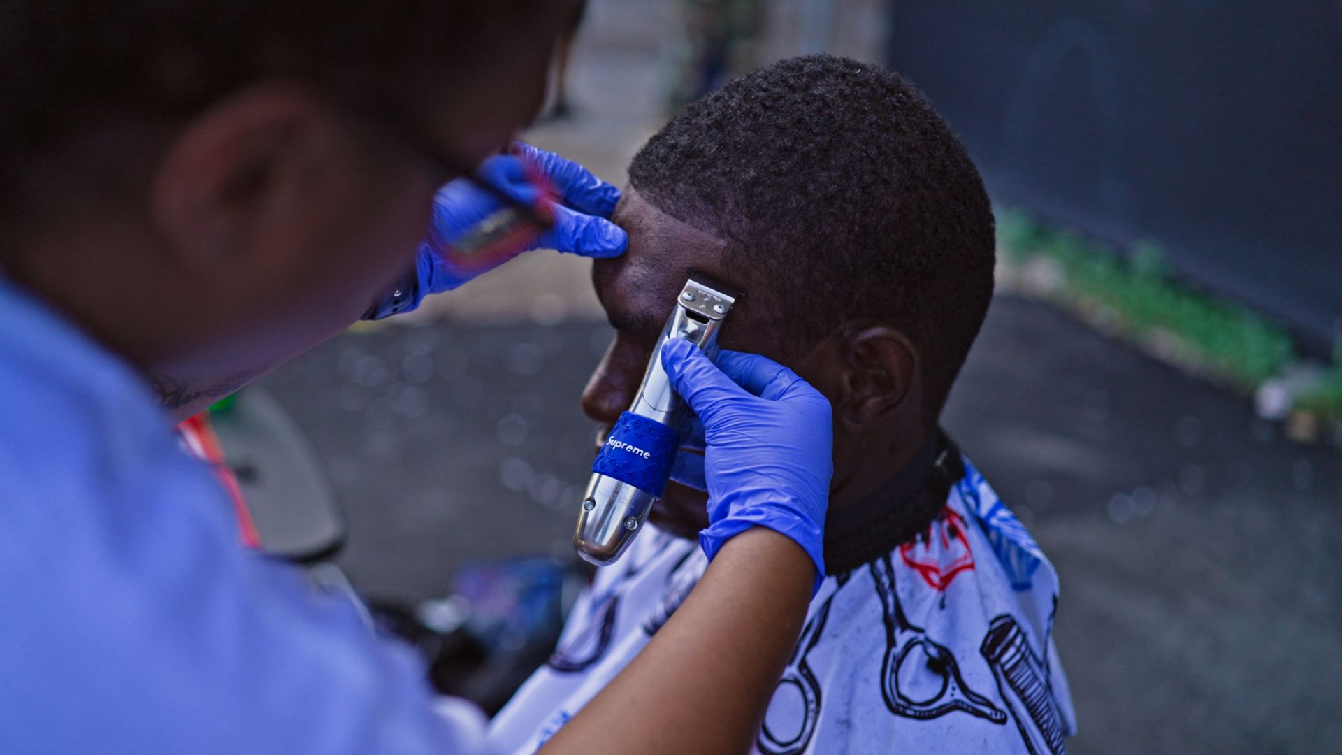 A man is getting his hair cut by a woman wearing blue gloves.