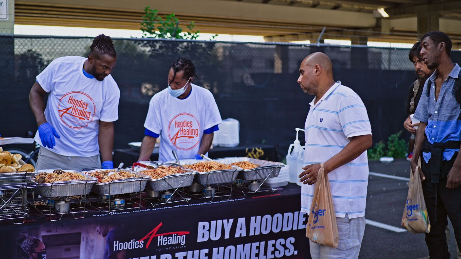 A group of men are standing around a table with food on it.