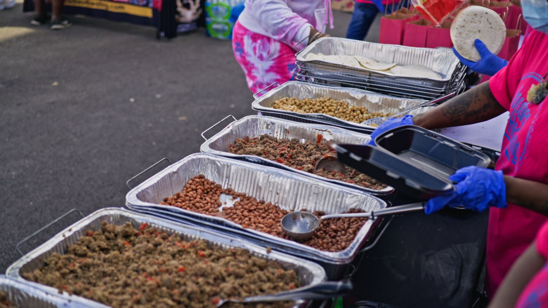 A group of people are standing around a table filled with trays of food.