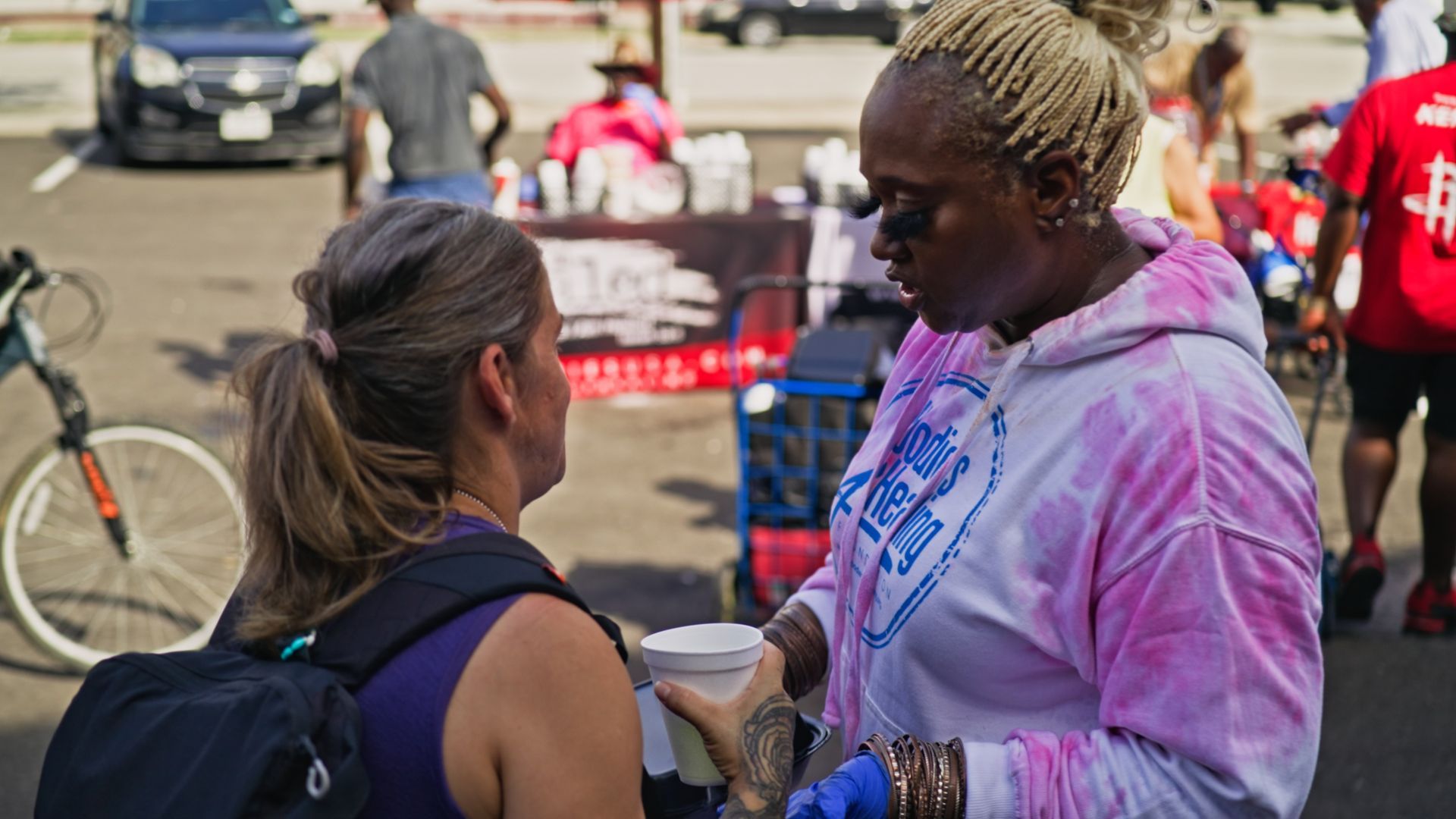 A woman in a pink tie dye shirt is talking to another woman.